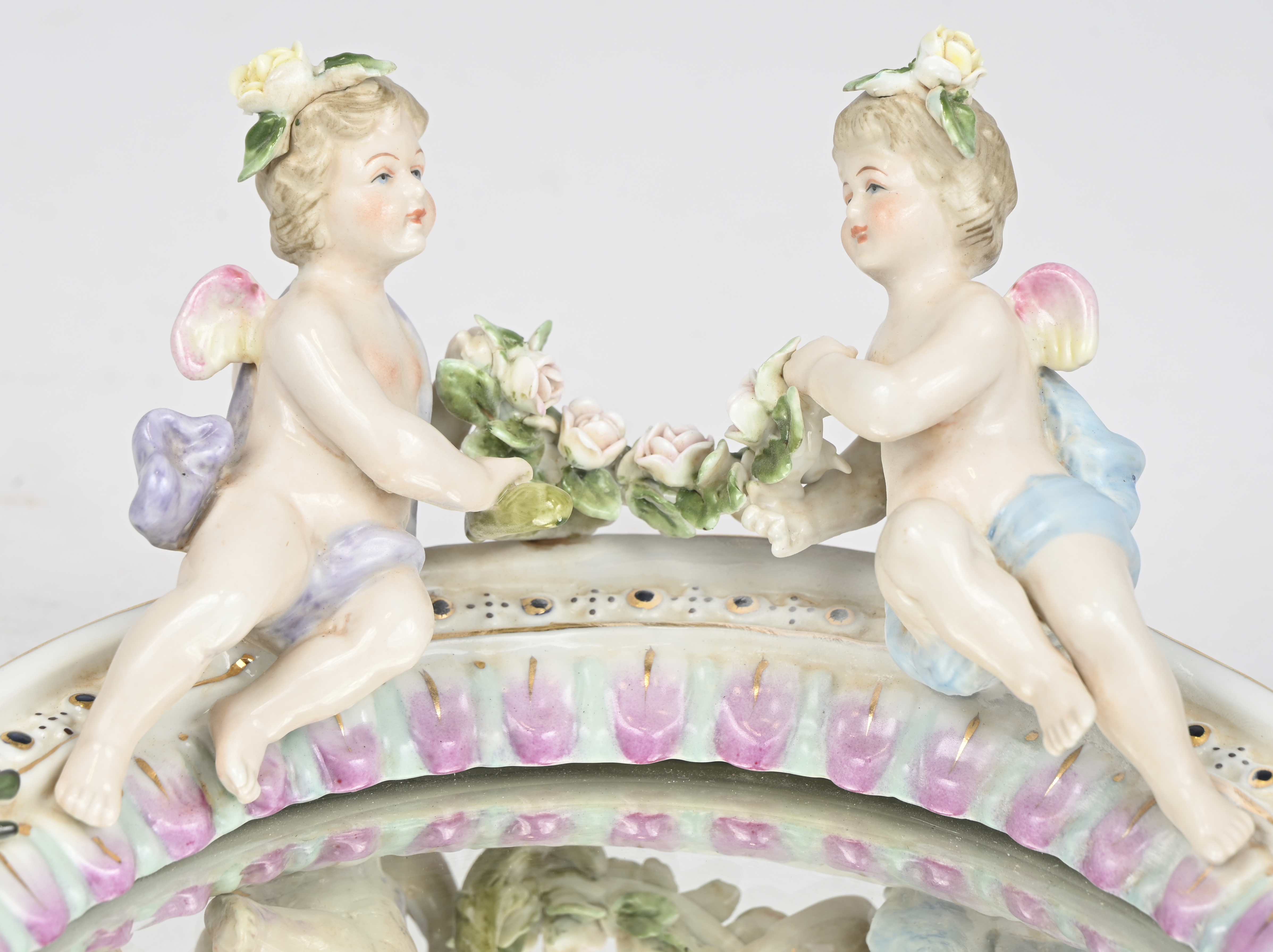 Een spiegeltje in porseleinen kader, met bloemen en engeltjes gedecoreerd. Gemerkt met gekruiste zwaarden boven een R Een spiegeltje in porseleinen kader, met bloemen en engeltjes gedecoreerd. Gemerkt met gekruiste zwaarden boven een R.