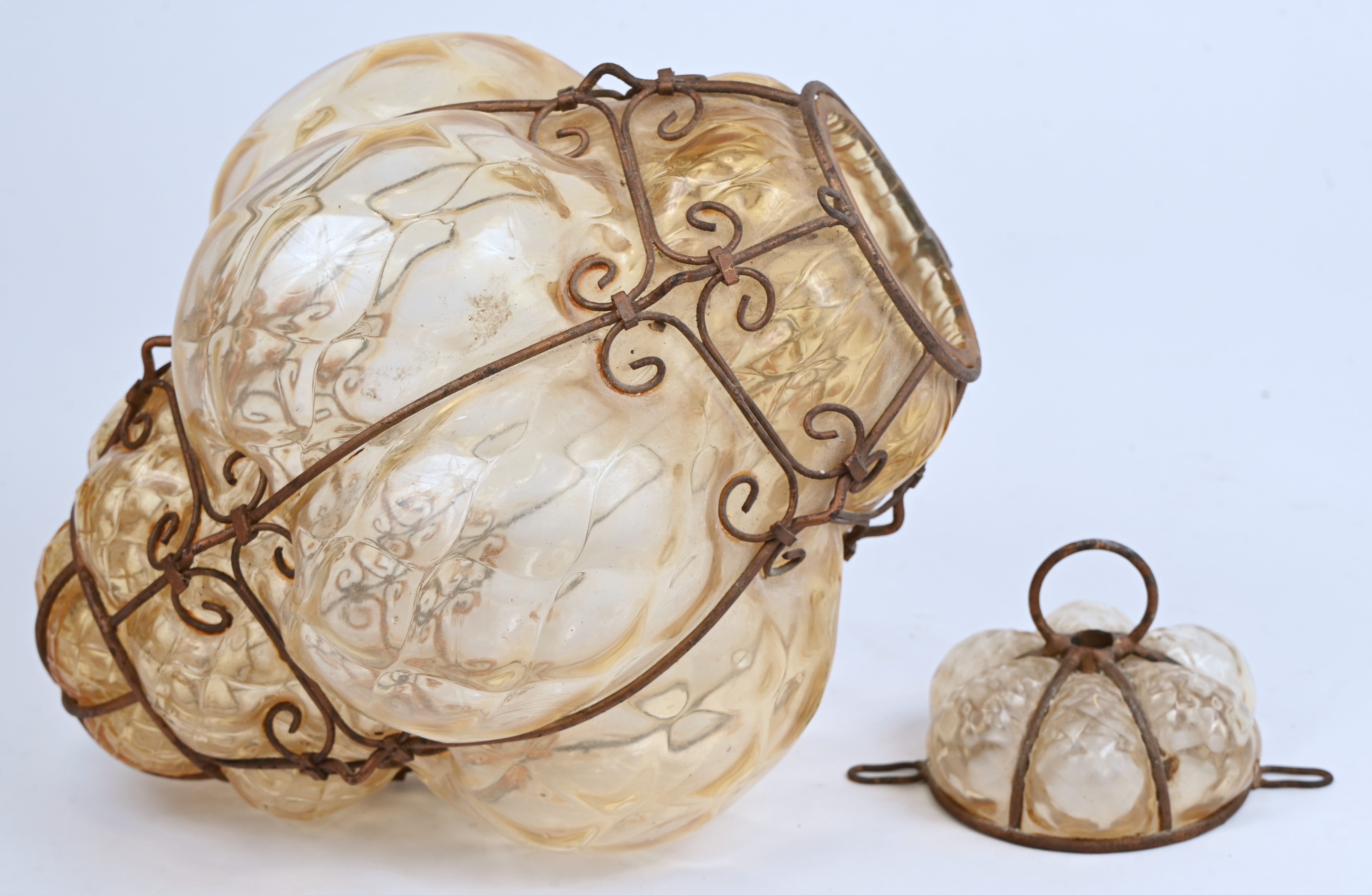 Een hallamp van beige geblazen glas. In smeedijzeren montuur. Eerste helft XXste eeuw Een hallamp van beige geblazen glas. In smeedijzeren montuur. Eerste helft XXste eeuw.