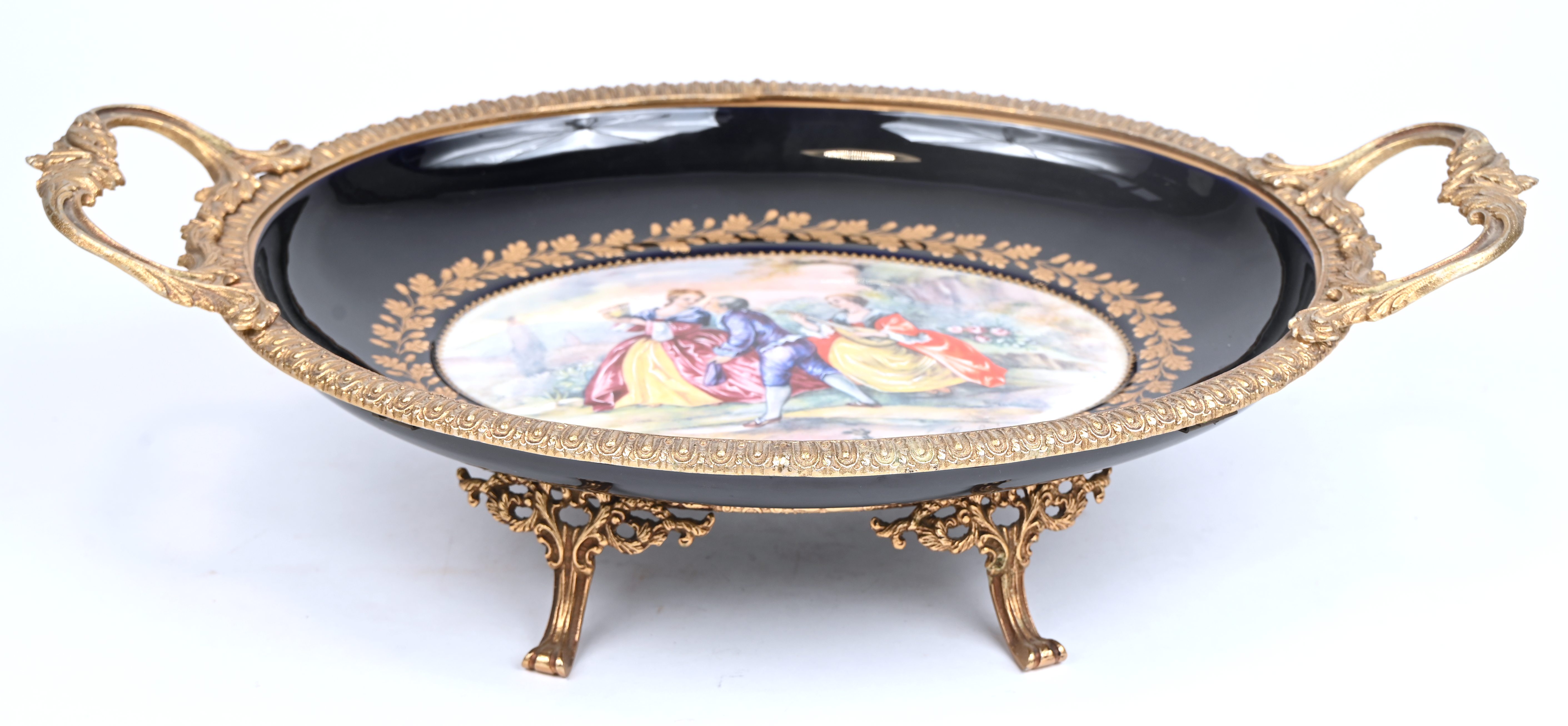 Een porseleinen schaal met messing handvatten en onderstel, onderaan opschrift’A.C.F. Décor bleu Sèvres - fait à la main Een porseleinen schaal met messing handvatten en onderstel, onderaan opschrift’A.C.F. Décor bleu Sèvres - fait à la main.