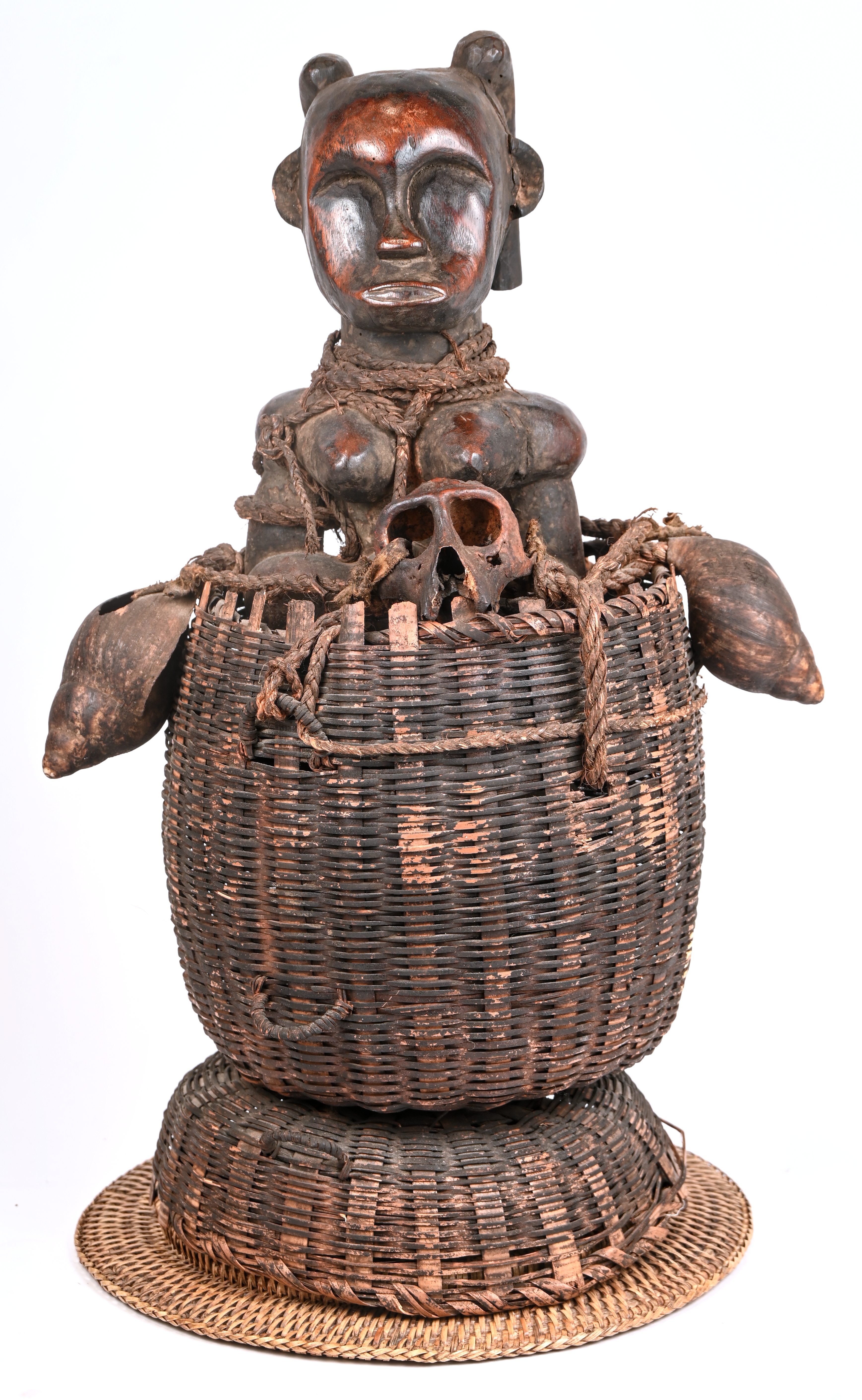 Een Afrikaans fetisjbeeld in een gevlochten mand, gedecoreerd met schelpen en apenschedels Een Afrikaans fetisjbeeld in een gevlochten mand, gedecoreerd met schelpen en apenschedels.