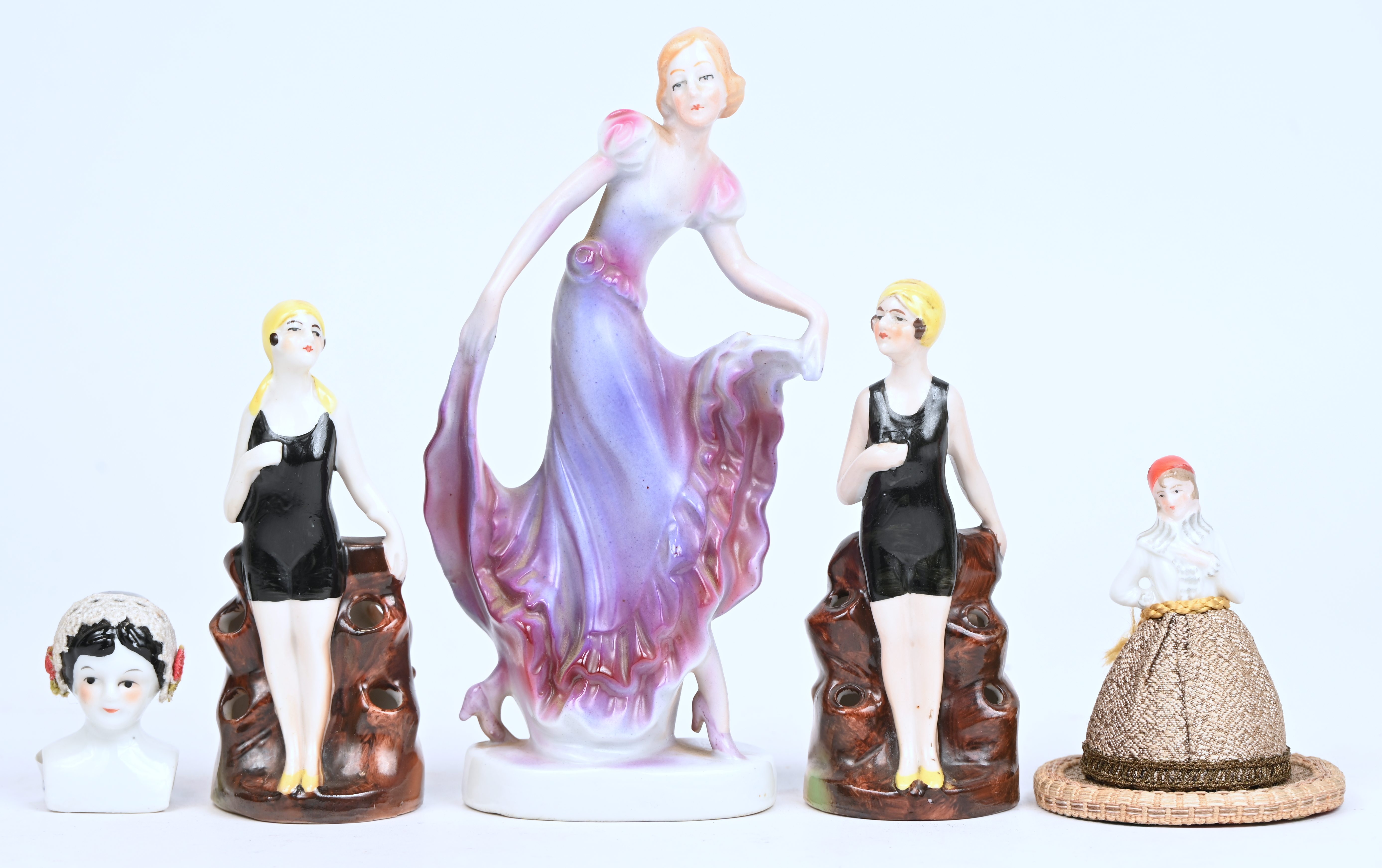 Een lot art-deco porselein bestaande uit een beeldje, 2 solifleurs met dames in badpak, een hoofdje en een half-doll/speldenkussen Een lot art-deco porselein bestaande uit een beeldje, 2 solifleurs met dames in badpak, een hoofdje en een half-doll/speldenkussen.