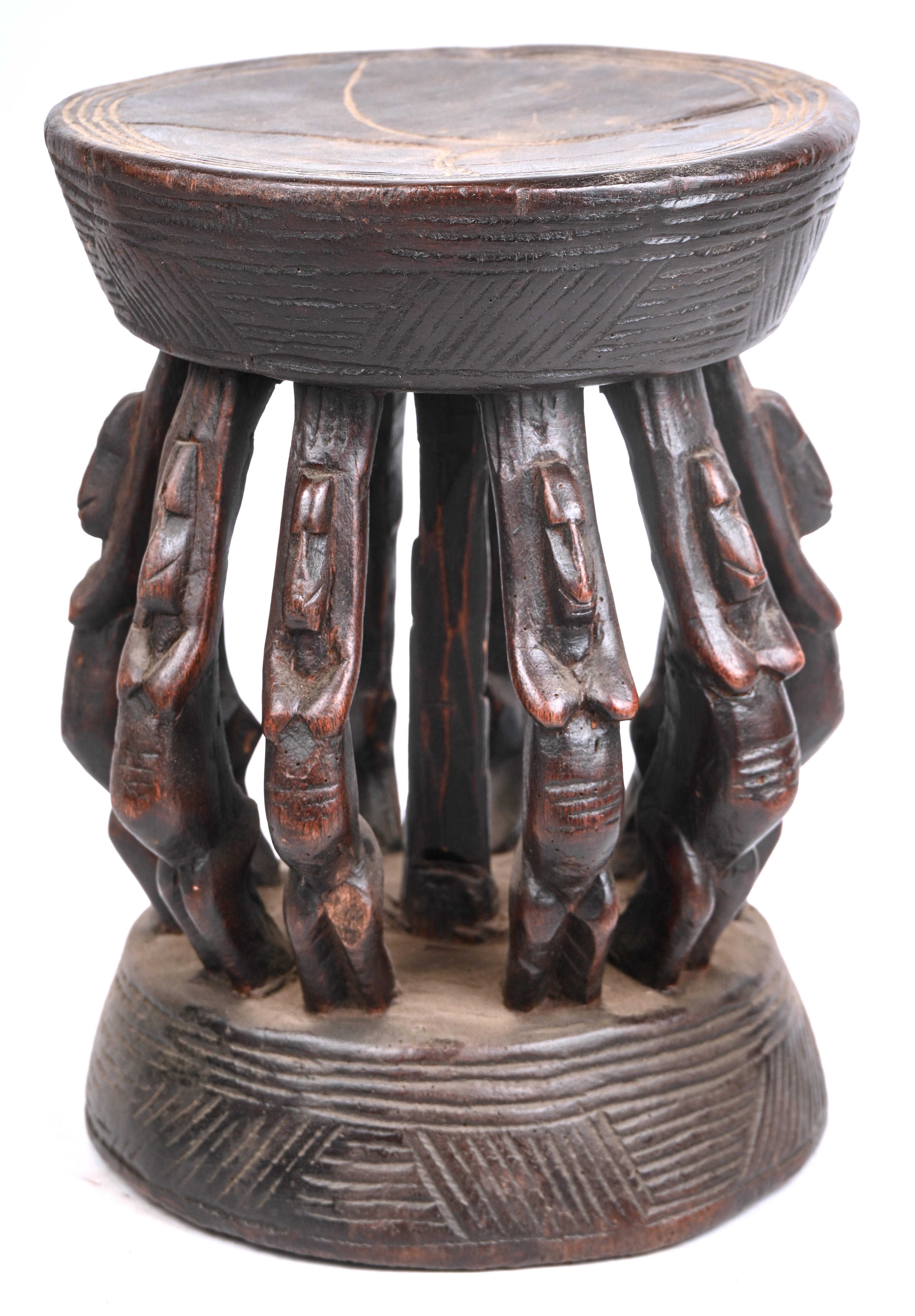 Een Afrikaans houten krukje, het zitvlak gedragen door tien dansende vrouwenfiguren Een Afrikaans houten krukje, het zitvlak gedragen door tien dansende vrouwenfiguren.