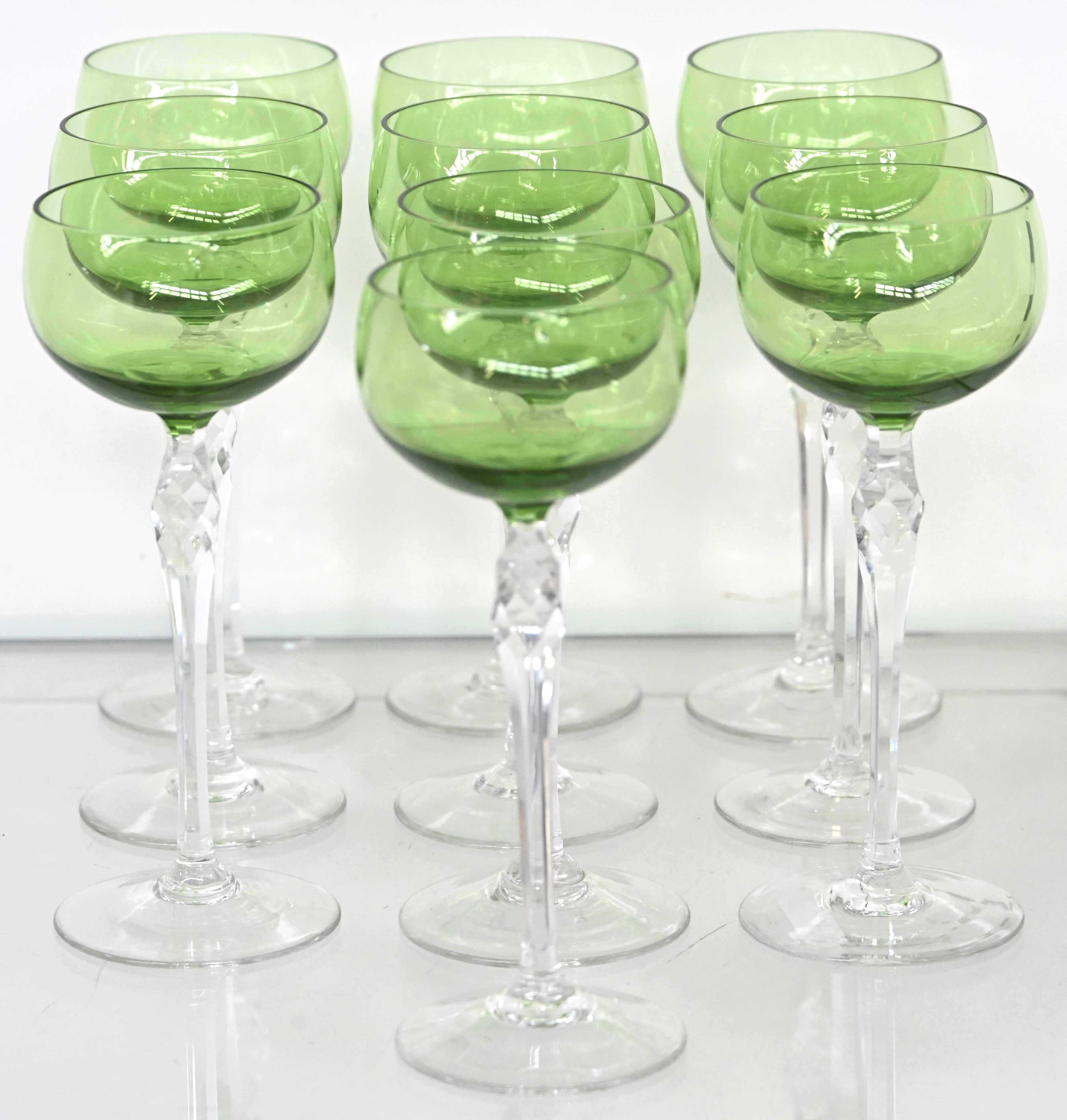 Tien kristallen glazen met geslepen stam en groene kelk Tien kristallen glazen met geslepen stam en groene kelk.