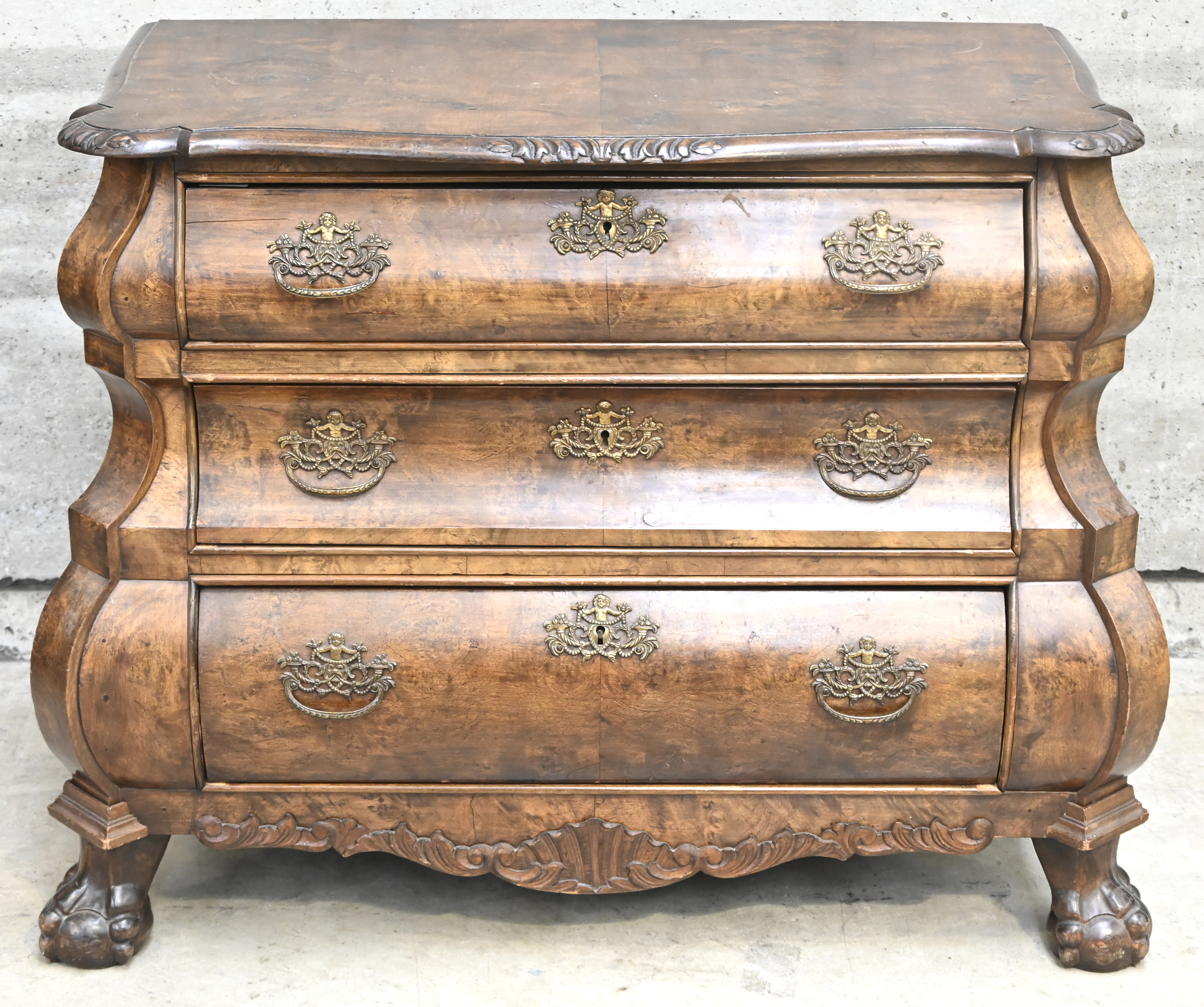Een buikcommode op klauwpoten, met drie laden. Met messing beslag en wortelfineer Een buikcommode op klauwpoten, met drie laden. Met messing beslag en wortelfineer.