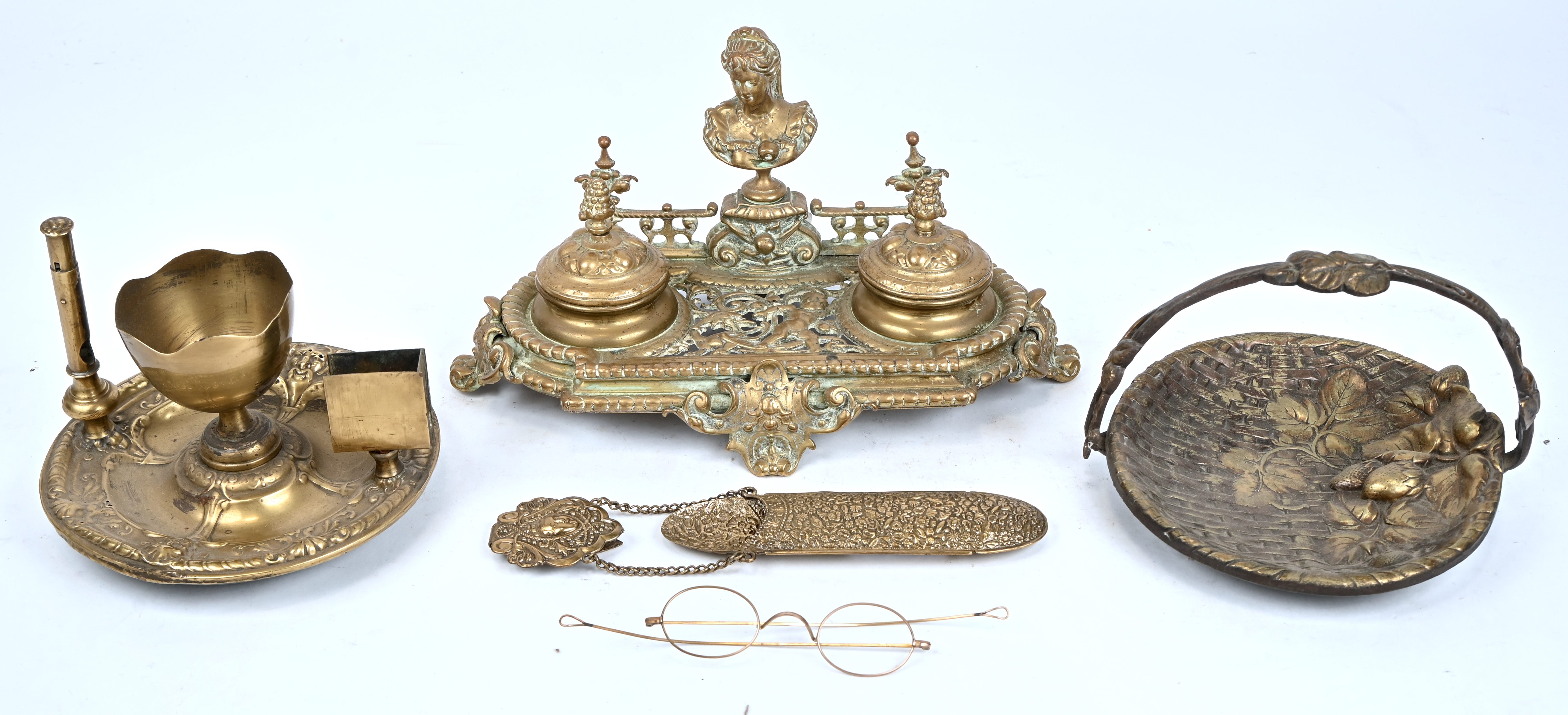 Een gevarieerd lot koper voor het bureau bestaande uit een inktpothouder, een rokersset, een vide-poche en een brillenhouder met bril Een gevarieerd lot koper voor het bureau bestaande uit een inktpothouder, een rokersset, een vide-poche en een brillenhouder met bril.