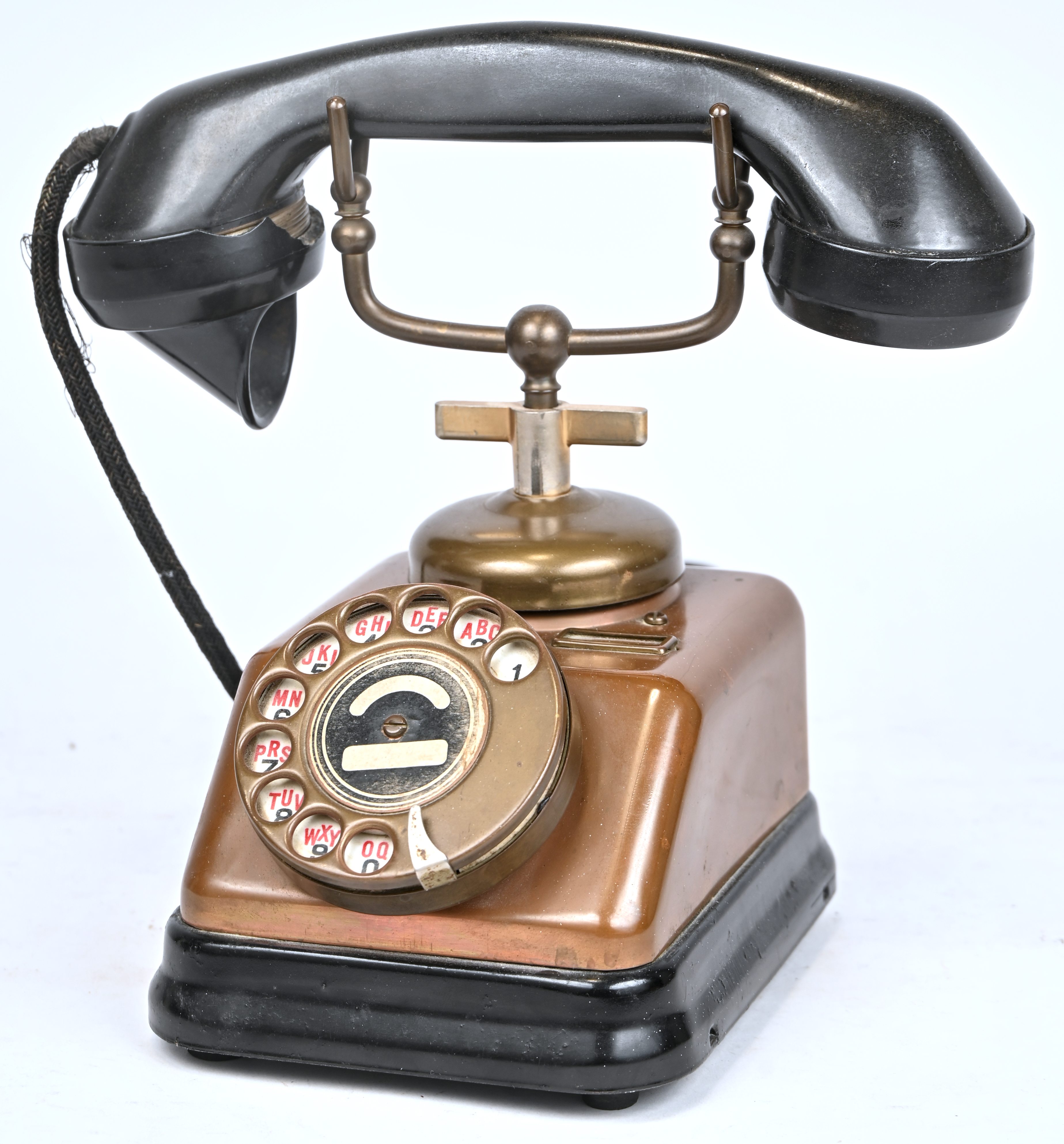 Een oude telefoon met draaischijf. Koper en bakeliet, met schade aan de hoorn Een oude telefoon met draaischijf. Koper en bakeliet, met schade aan de hoorn.