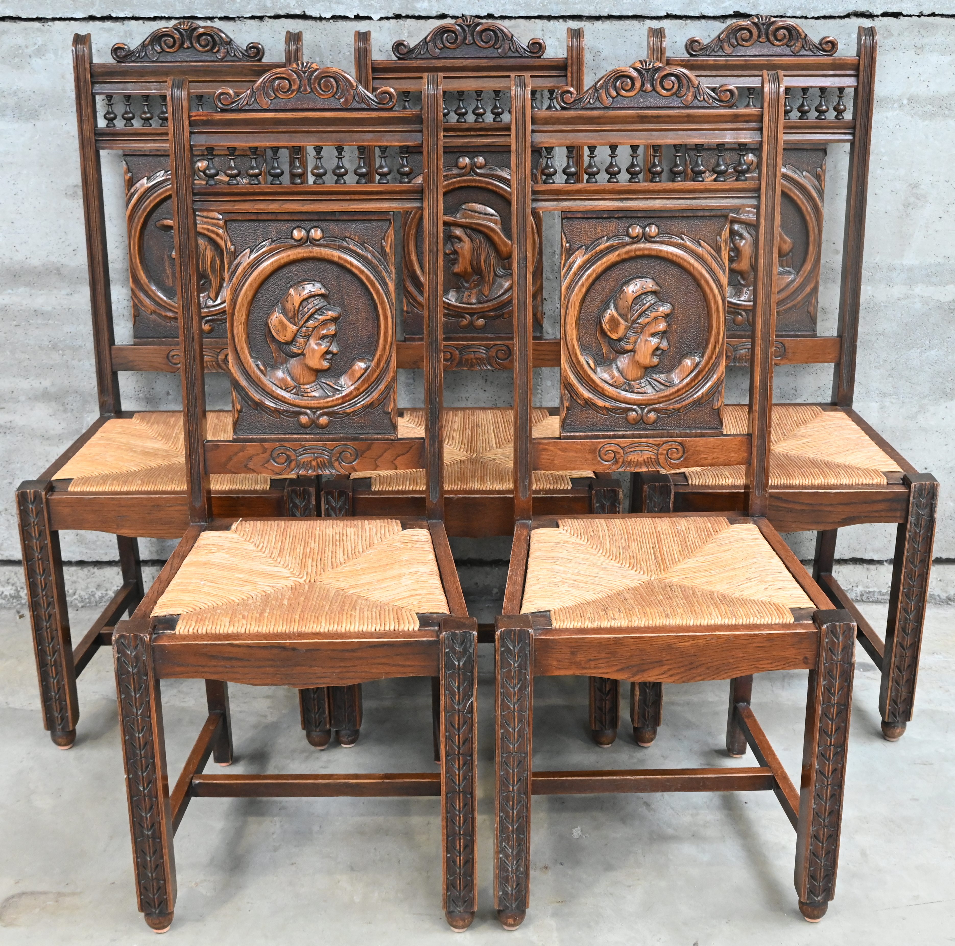 Een set van vijf eikenhouten stoelen met gevlochten zit en een gesculpteerd rugpaneel. Drie met een mannenportret en twee met een vrouwenportret. Zithoogte 45 cm Een set van vijf eikenhouten stoelen met gevlochten zit en een gesculpteerd rugpaneel. Drie met een mannenportret en twee met een vrouwenportret. Zithoogte 45 cm.