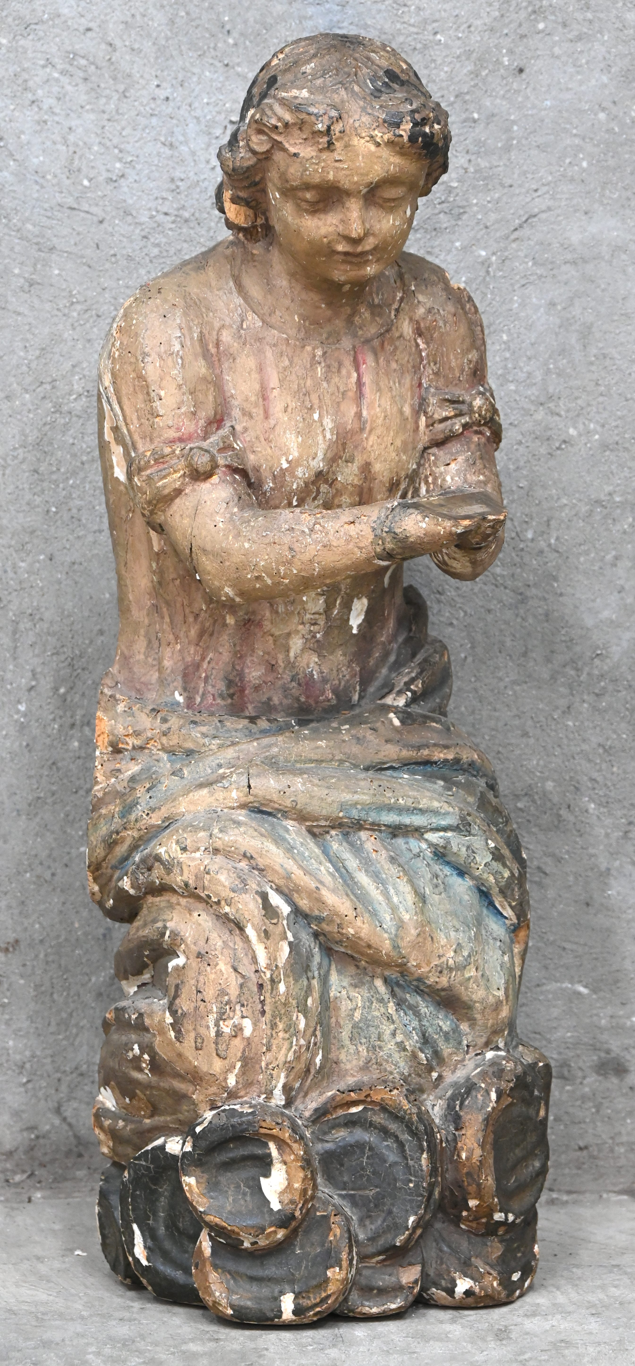 Een antiek houten beeld van een engel, knielend op een wolk. Met resten van polychrome beschildering. Draagt een label verwijzend naar de abdij van Villers. Vermoedelijk deel van van een altaarstuk, 18e eeuw Een antiek houten beeld van een engel, knielend op een wolk. Met resten van polychrome beschildering. Draagt een label verwijzend naar de abdij van Villers. Vermoedelijk deel van van een altaarstuk, 18e eeuw.
