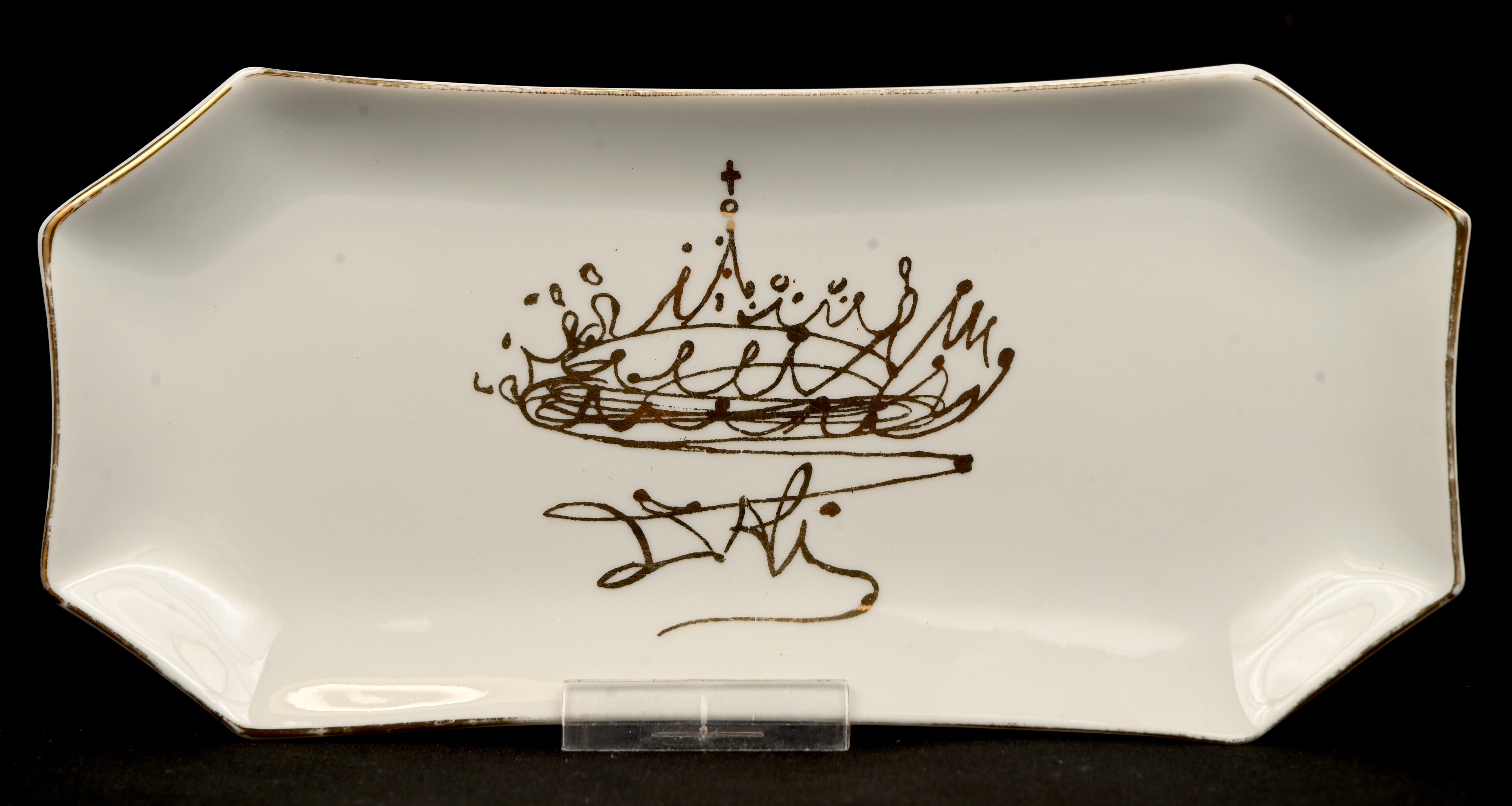 Een porseleinen schaaltje gedecoreerd met een kroon, naar werk van Dali. Onderaan gemerkt ‘Distribucions d’Art Surrealista’ Een porseleinen schaaltje gedecoreerd met een kroon, naar werk van Dali. Onderaan gemerkt ‘Distribucions d’Art Surrealista’.