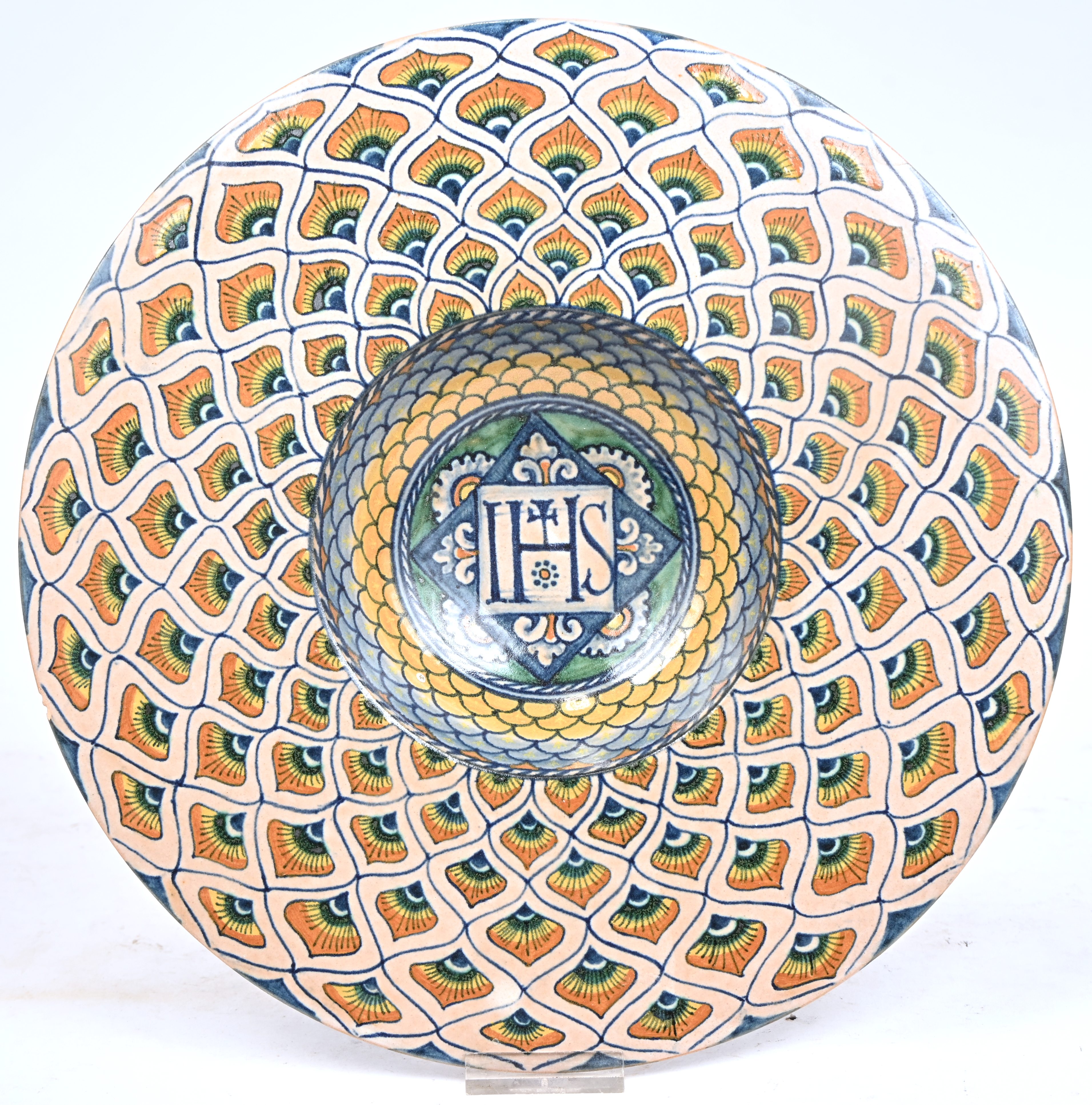 Een Deruta sierbord met pauwenoog decor. Met centraal een IHS christogram. Onderaan gemerkt ‘AA’. Schilferschade aan de rand Een Deruta sierbord met pauwenoog decor. Met centraal een IHS christogram. Onderaan gemerkt ‘AA’. Schilferschade aan de rand.