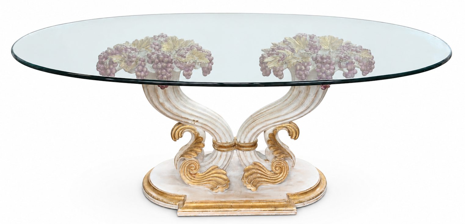 Een vintage tafel, polychrome gesculpteerde houten voet met druiventrossen en ovaal glazen blad Een vintage tafel, polychrome gesculpteerde houten voet met druiventrossen en ovaal glazen blad.