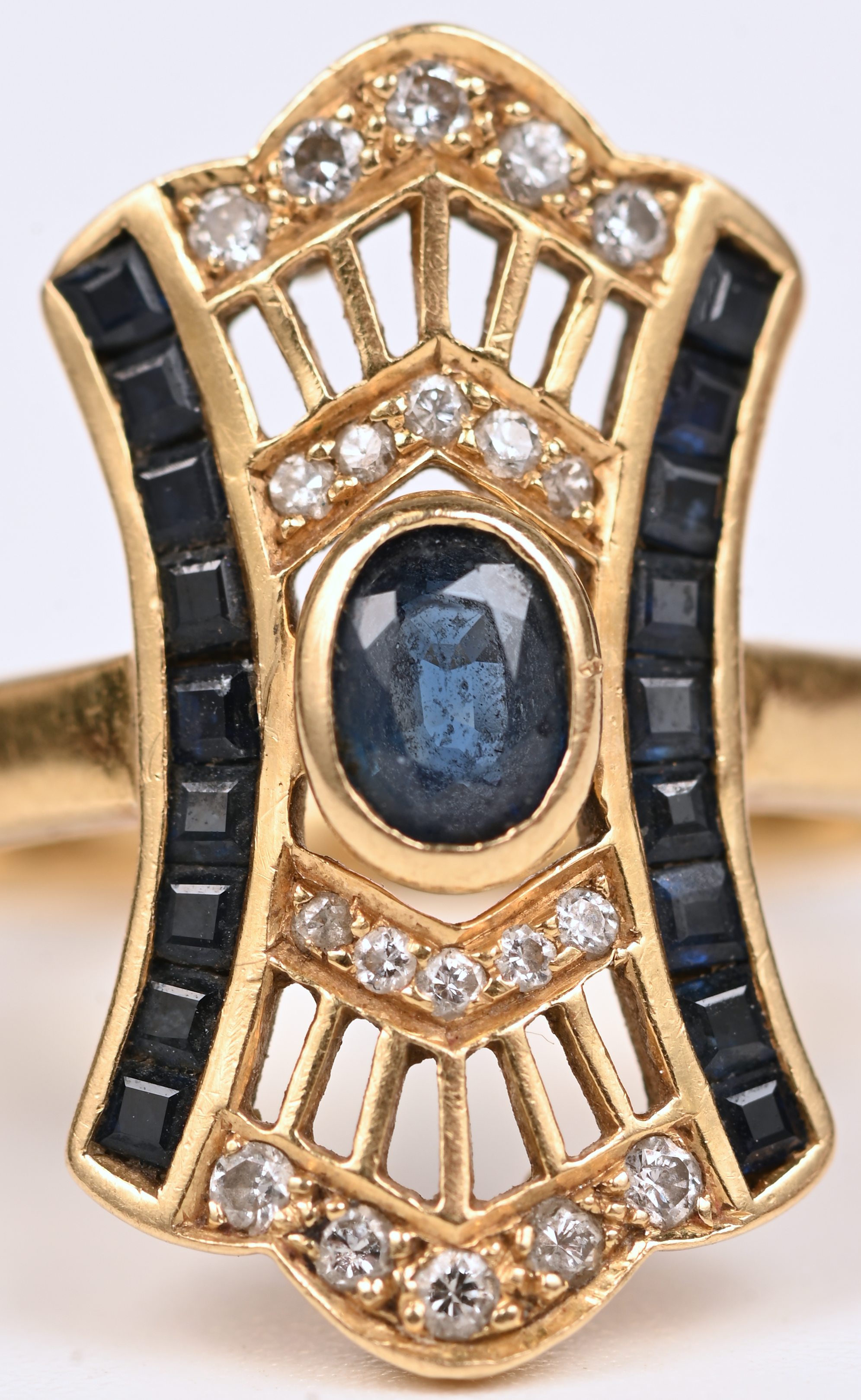Een 18 kt art deco geelgouden ring bezet met een centrale saffier van +- 0,20 ct. en gekalibreerde saffieren met een gezamenlijk gewicht van +- 0,30 ct. en diamanten oude slijp met een gezamenlijk gewicht van +- 0,20 ct Een 18 kt art deco geelgouden ring bezet met een centrale saffier van +- 0,20 ct. en gekalibreerde saffieren met een gezamenlijk gewicht van +- 0,30 ct. en diamanten oude slijp met een gezamenlijk gewicht van +- 0,20 ct.