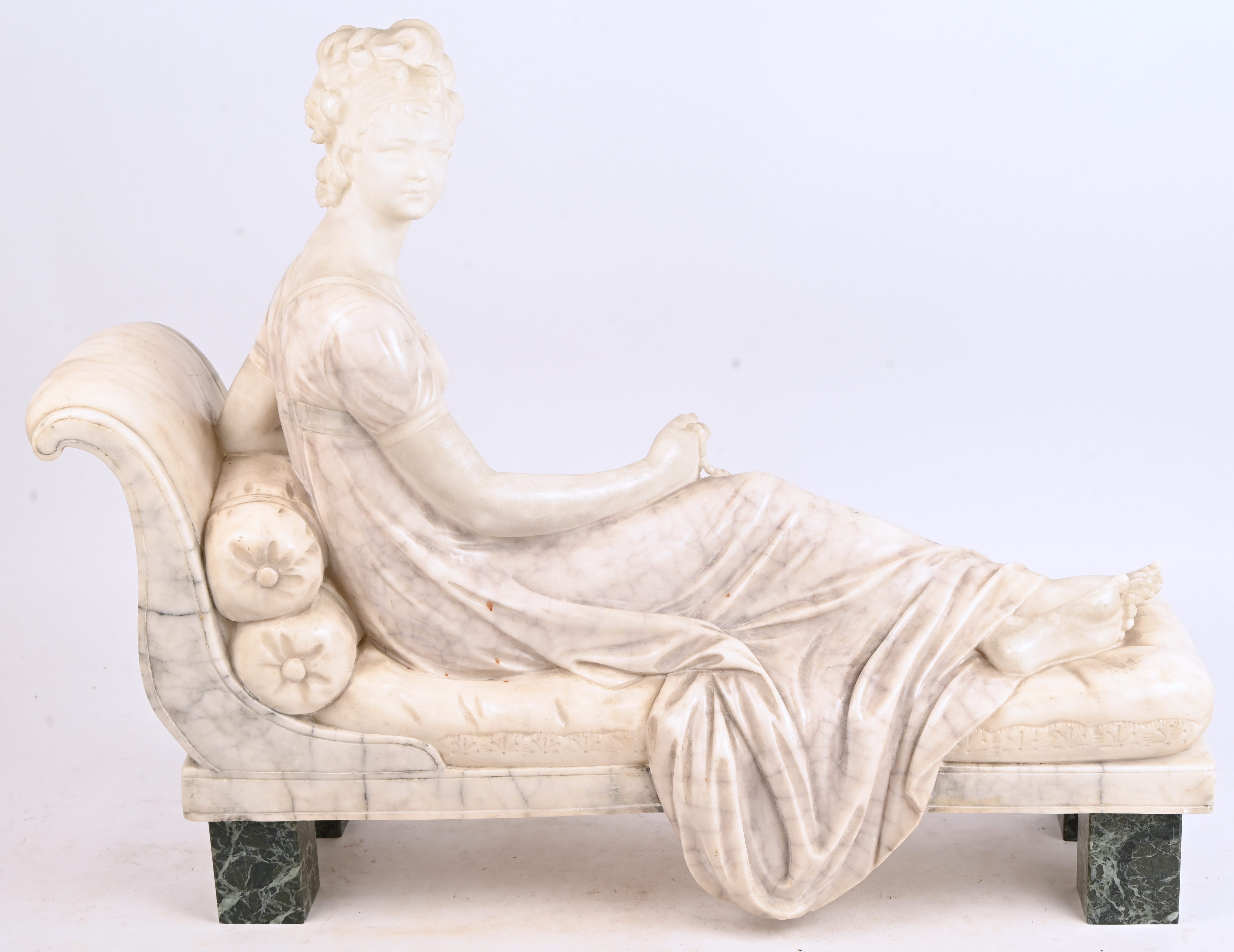 “Jongedame op chaise longue”, een albasten beeld op groen marmeren voetjes “Jongedame op chaise longue”, een albasten beeld op groen marmeren voetjes.