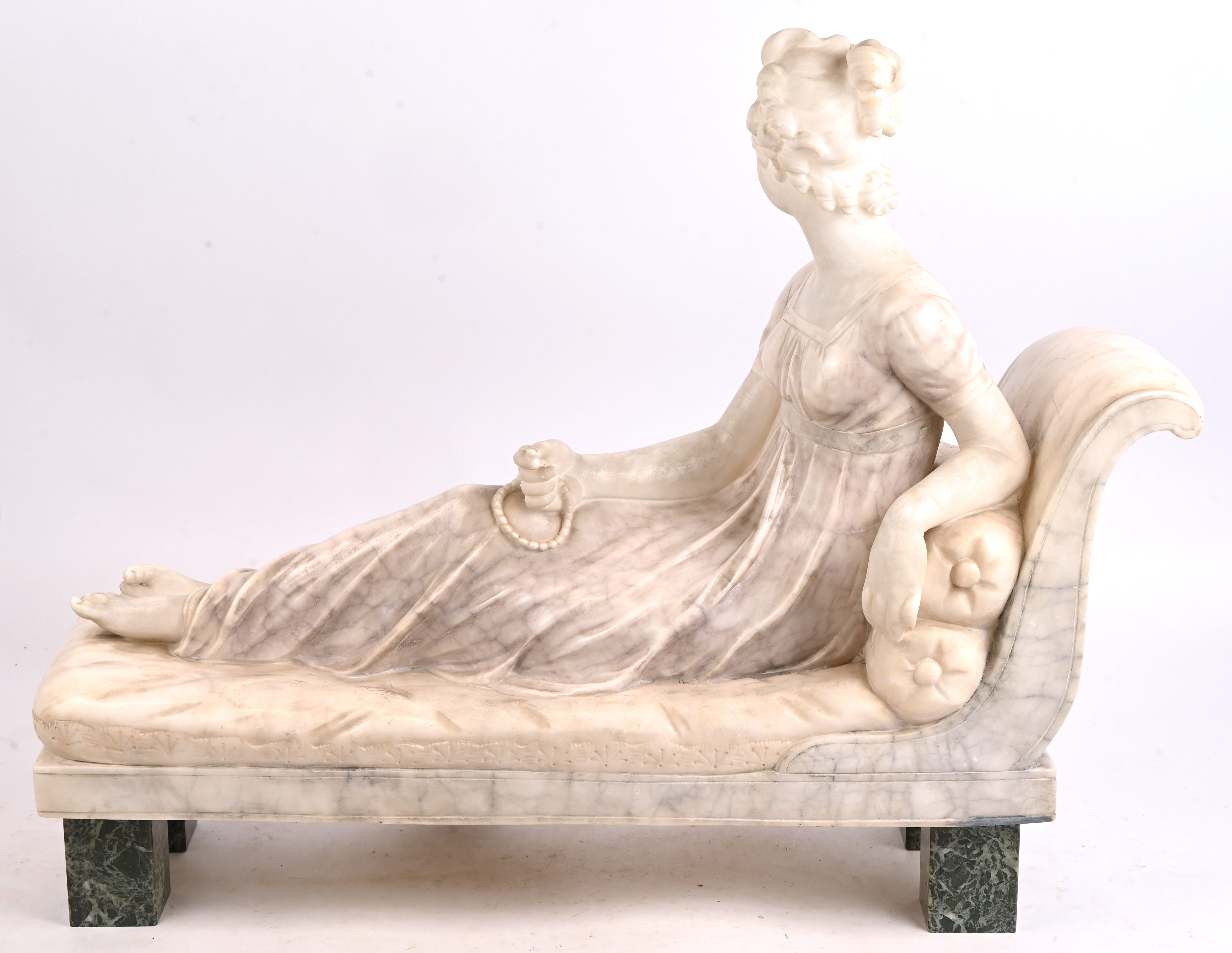 “Jongedame op chaise longue”, een albasten beeld op groen marmeren voetjes “Jongedame op chaise longue”, een albasten beeld op groen marmeren voetjes.