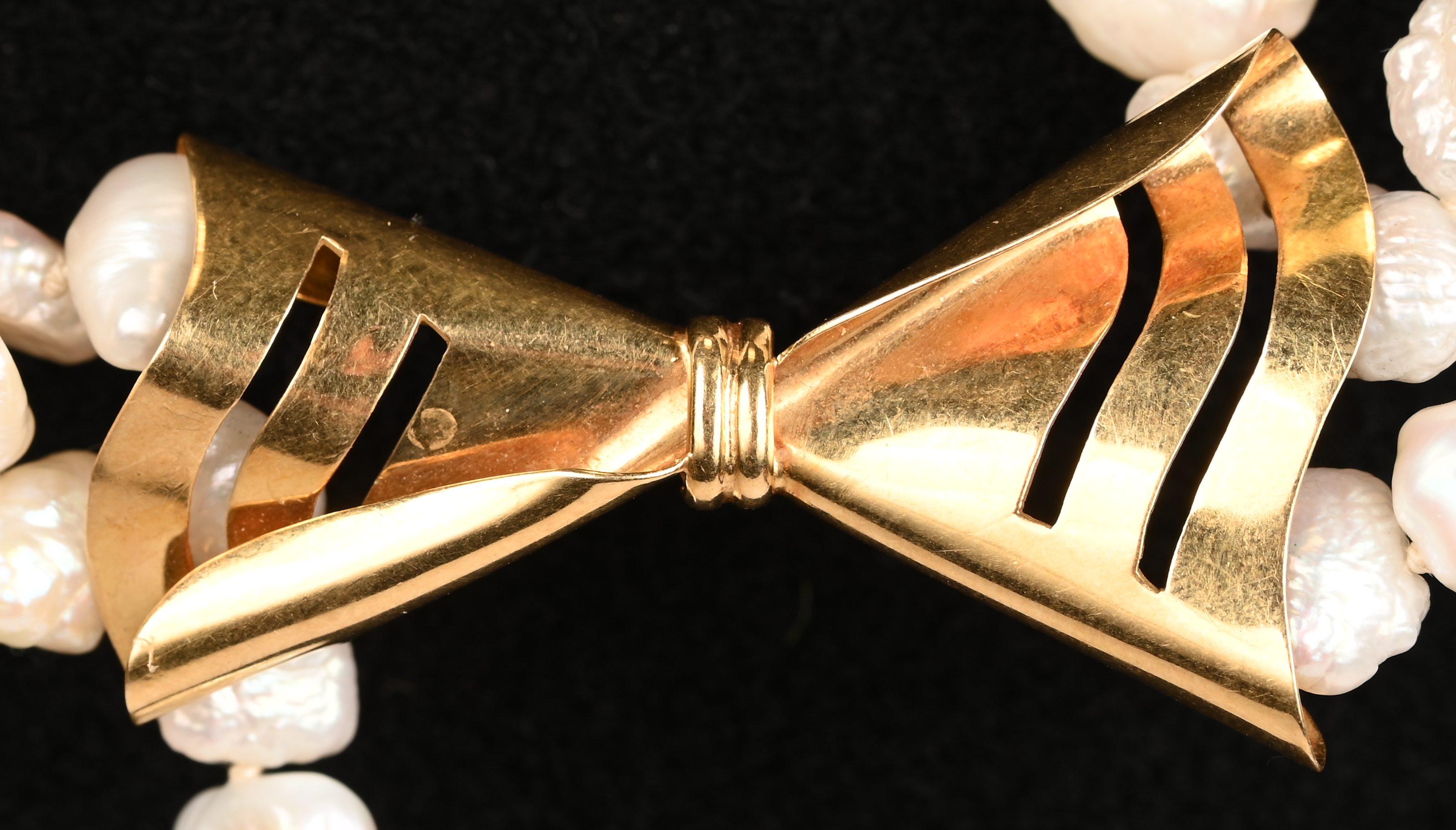Een drie rijen parelhalssnoer met 18 karaats geelgouden hanger in de vorm van een strik. (één rij te los) Een drie rijen parelhalssnoer met 18 karaats geelgouden hanger in de vorm van een strik. (één rij te los).