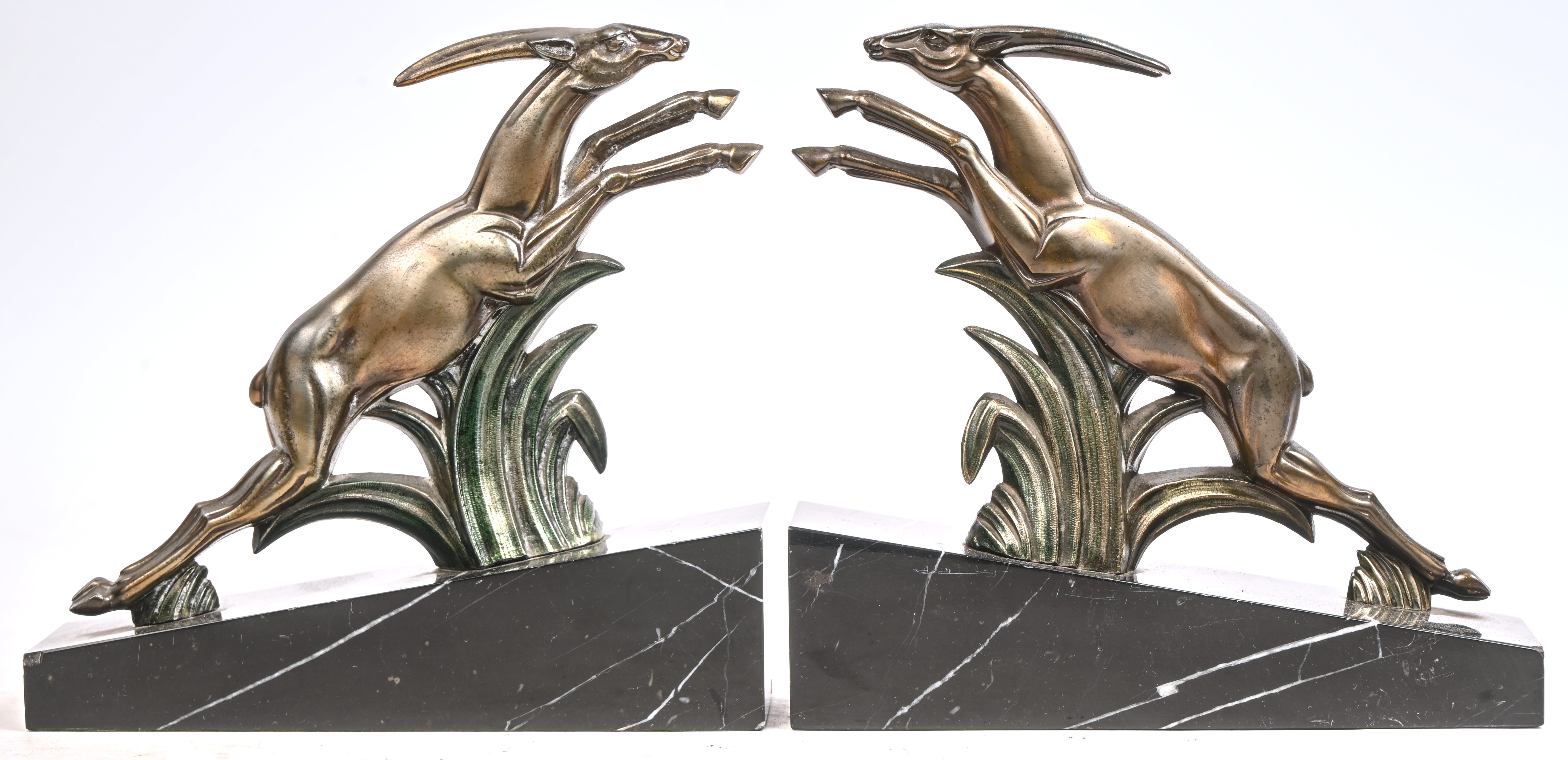 Een paar Art-Deco boekensteunen. Gevormd als springbokken, bronskleurig gepatineerd zamak op zwart marmeren voet. Minieme schade aan de basis Een paar Art-Deco boekensteunen. Gevormd als springbokken, bronskleurig gepatineerd zamak op zwart marmeren voet. Minieme schade aan de basis.