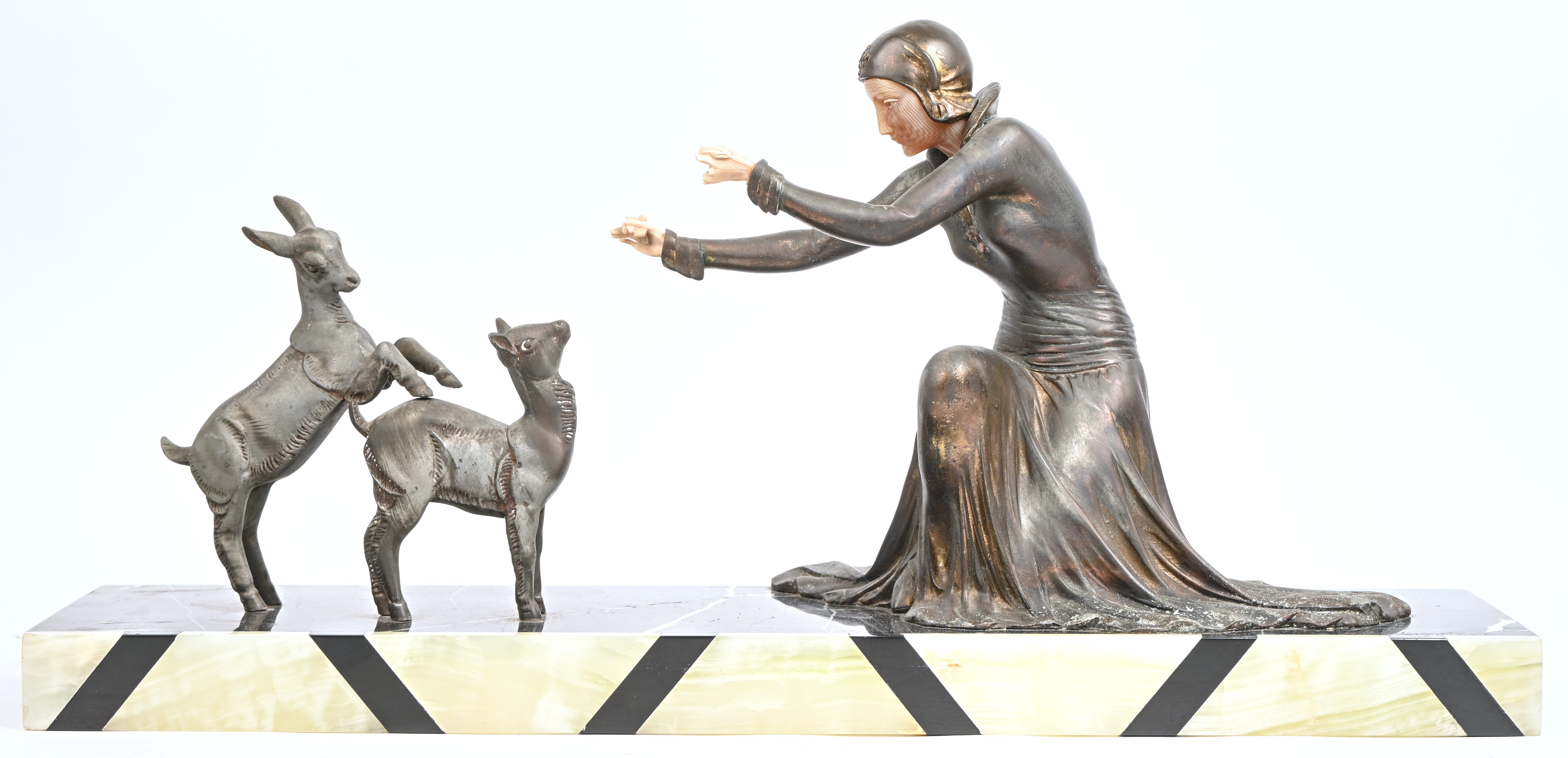 ‘Jonge vrouw met twee geitjes’, een art-deco beeld van gepatineerd zamac en kunsthars. Gesigneerd op de marmeren voet. Van het linkerhand zijn enkele vingers manco ‘Jonge vrouw met twee geitjes’, een art-deco beeld van gepatineerd zamac en kunsthars. Gesigneerd op de marmeren voet. Van het linkerhand zijn enkele vingers manco.