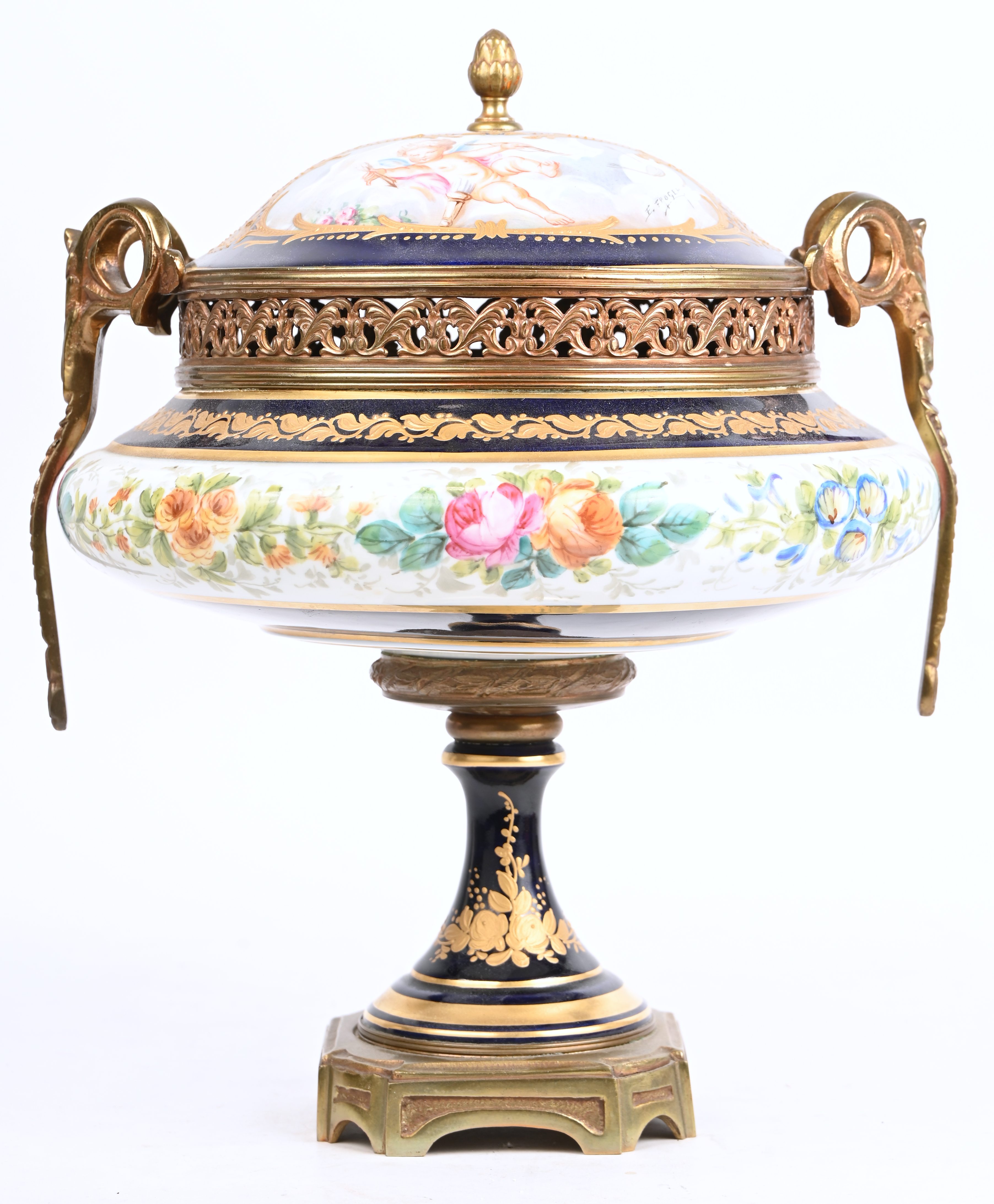 Een porseleinen coupe met deksel op voet met een decor van engelen en bloemen, gemerkt Sèvres en gesigneerd E. Froger Een porseleinen coupe met deksel op voet met een decor van engelen en bloemen, gemerkt Sèvres en gesigneerd E. Froger.