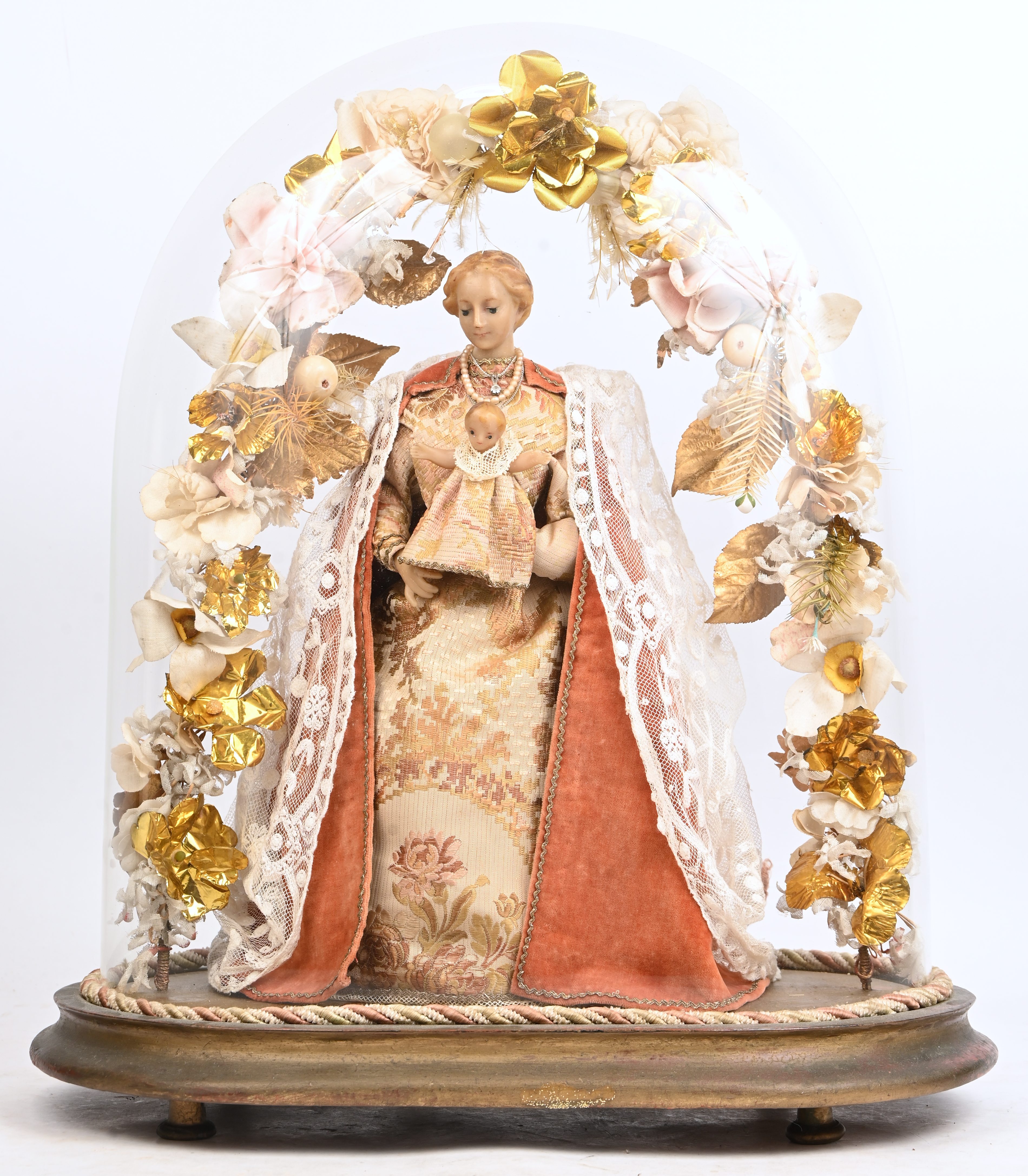 Een wassen Madonna met kind onder een boog van bloemen, in ovale glazen stolp Een wassen Madonna met kind onder een boog van bloemen, in ovale glazen stolp.