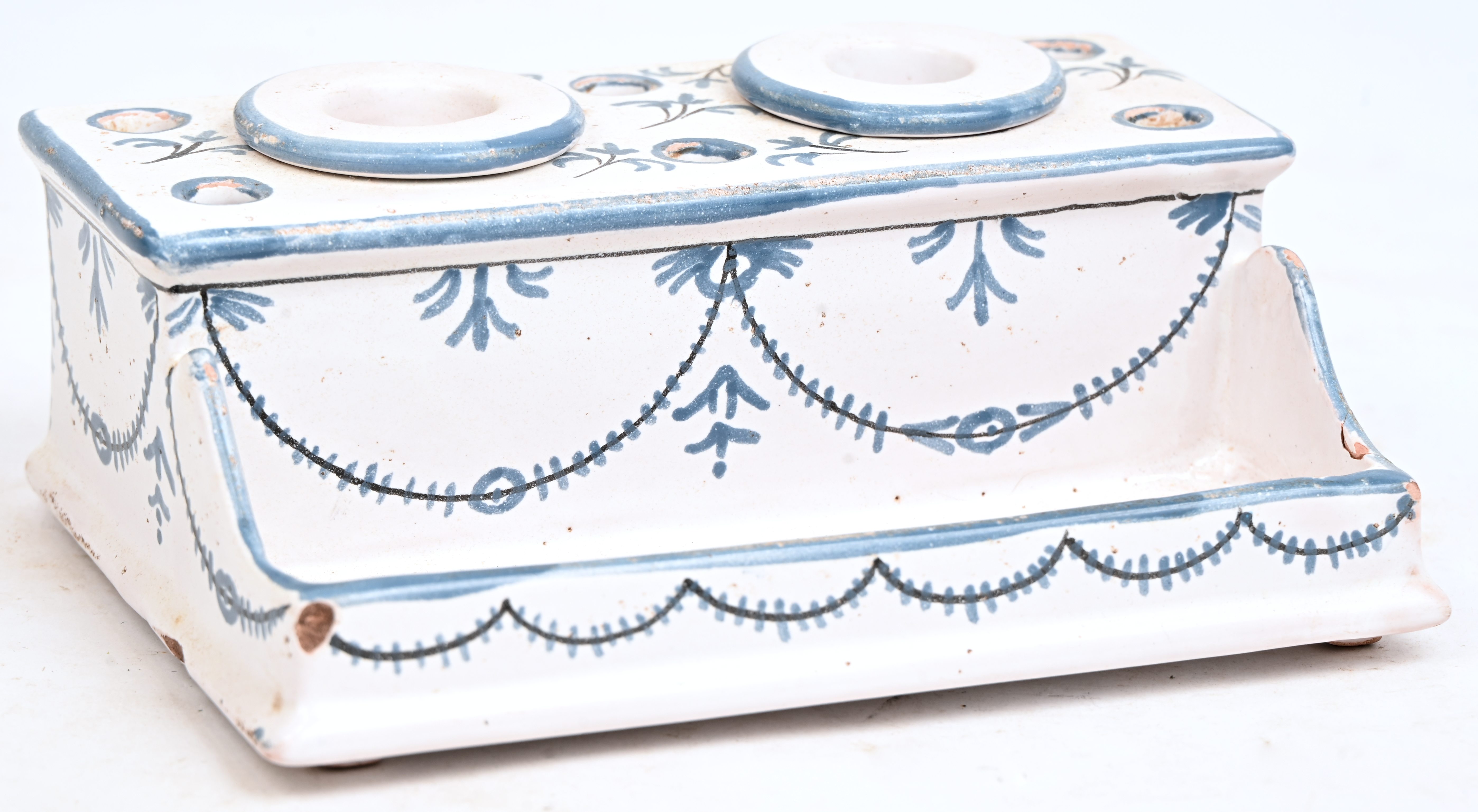 Een inktstelletje van blauw-wit geglazuurd aardewerk. Met twee inktpotjes, met herstelling en schilferschade Een inktstelletje van blauw-wit geglazuurd aardewerk. Met twee inktpotjes, met herstelling en schilferschade.