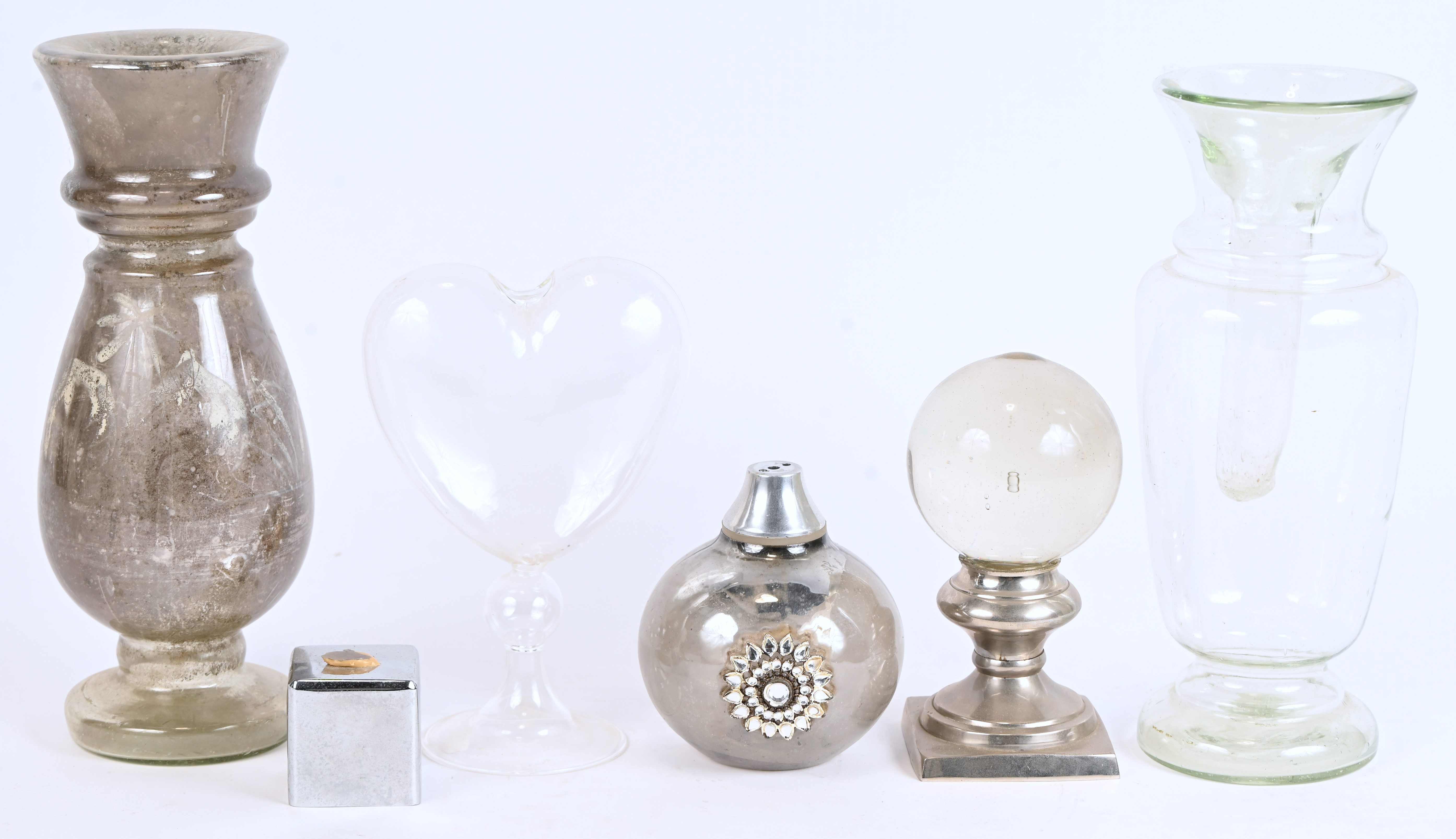 Een kristallen bol op metalen voet, twee glazen vazen, een mondgeblazen glazen hart, een met strass versierde glazen bol op metalen sokkel Een kristallen bol op metalen voet, twee glazen vazen, een mondgeblazen glazen hart, een met strass versierde glazen bol op metalen sokkel.