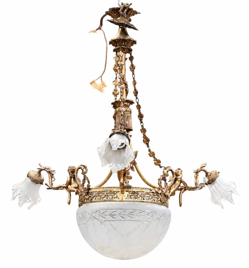 Een verguld bronzen luchter met drie lichtarmen, versierd met putti. Met gesatineerde glazen kapjes en geslepen centrale coupe Een verguld bronzen luchter met drie lichtarmen, versierd met putti. Met gesatineerde glazen kapjes en geslepen centrale coupe.