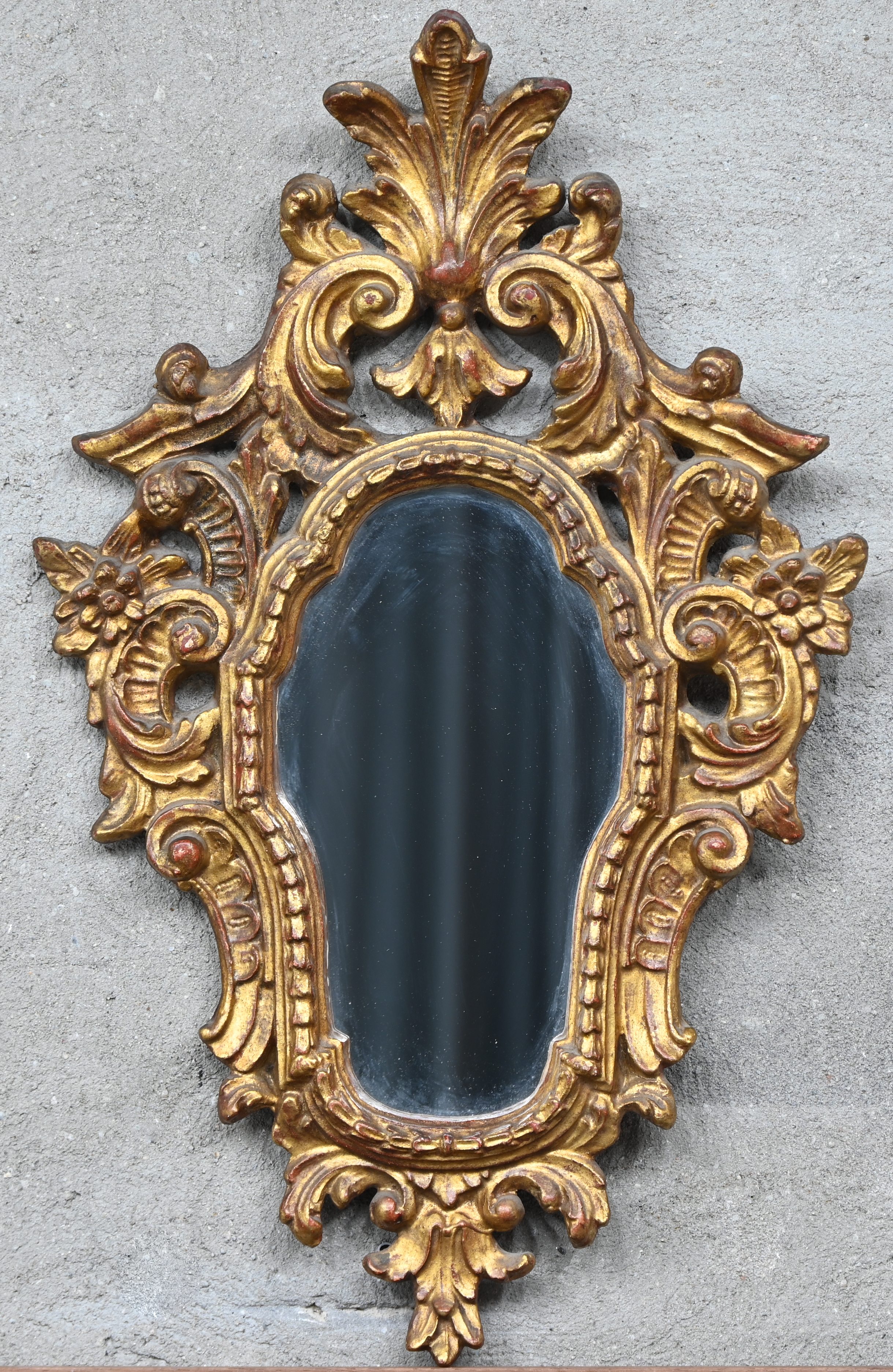 Een vlakke spiegel in een gesculteerde houten kader met kuif, goudkleurig. In Rococo stijl Een vlakke spiegel in een gesculteerde houten kader met kuif, goudkleurig. In Rococo stijl.
