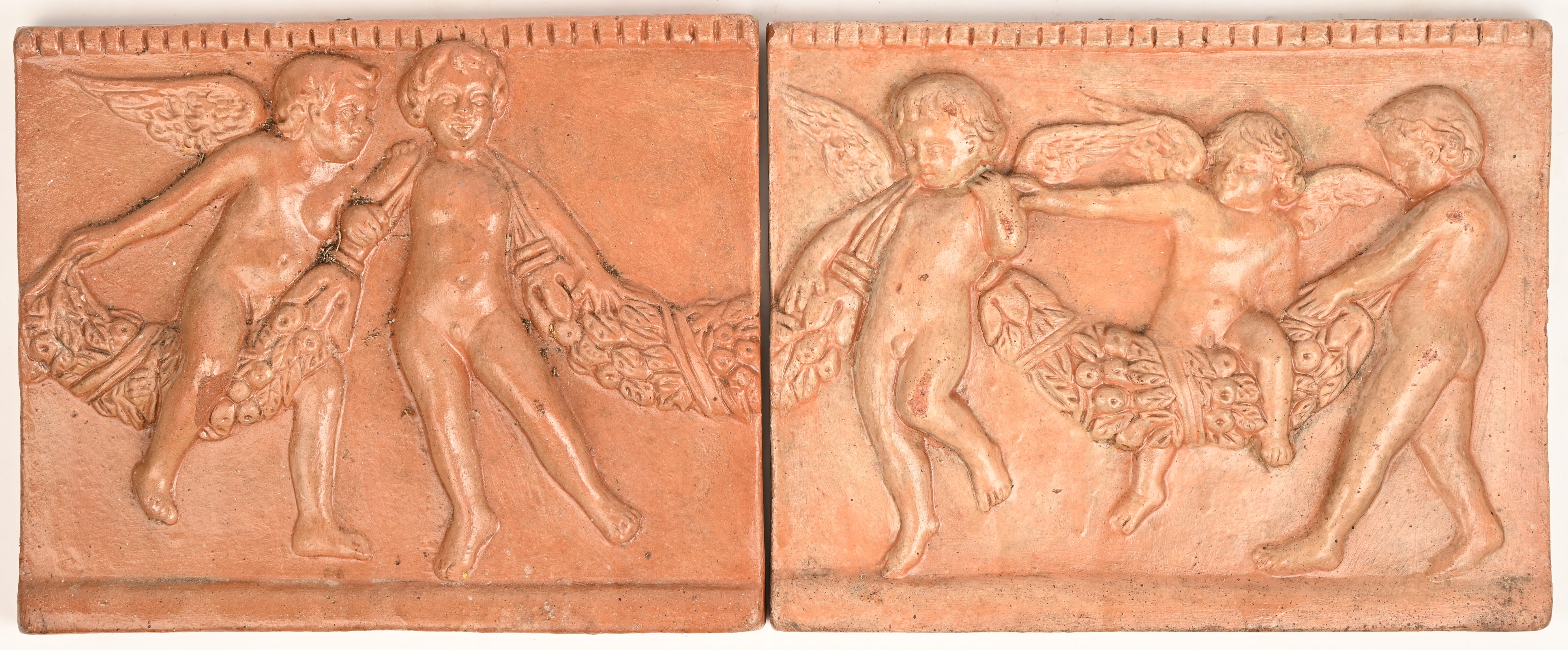 Twee terra cotta tegels met een decor in bas-reliëf van putti die een guirlande dragen. Met schade aan één putto Twee terra cotta tegels met een decor in bas-reliëf van putti die een guirlande dragen. Met schade aan één putto.