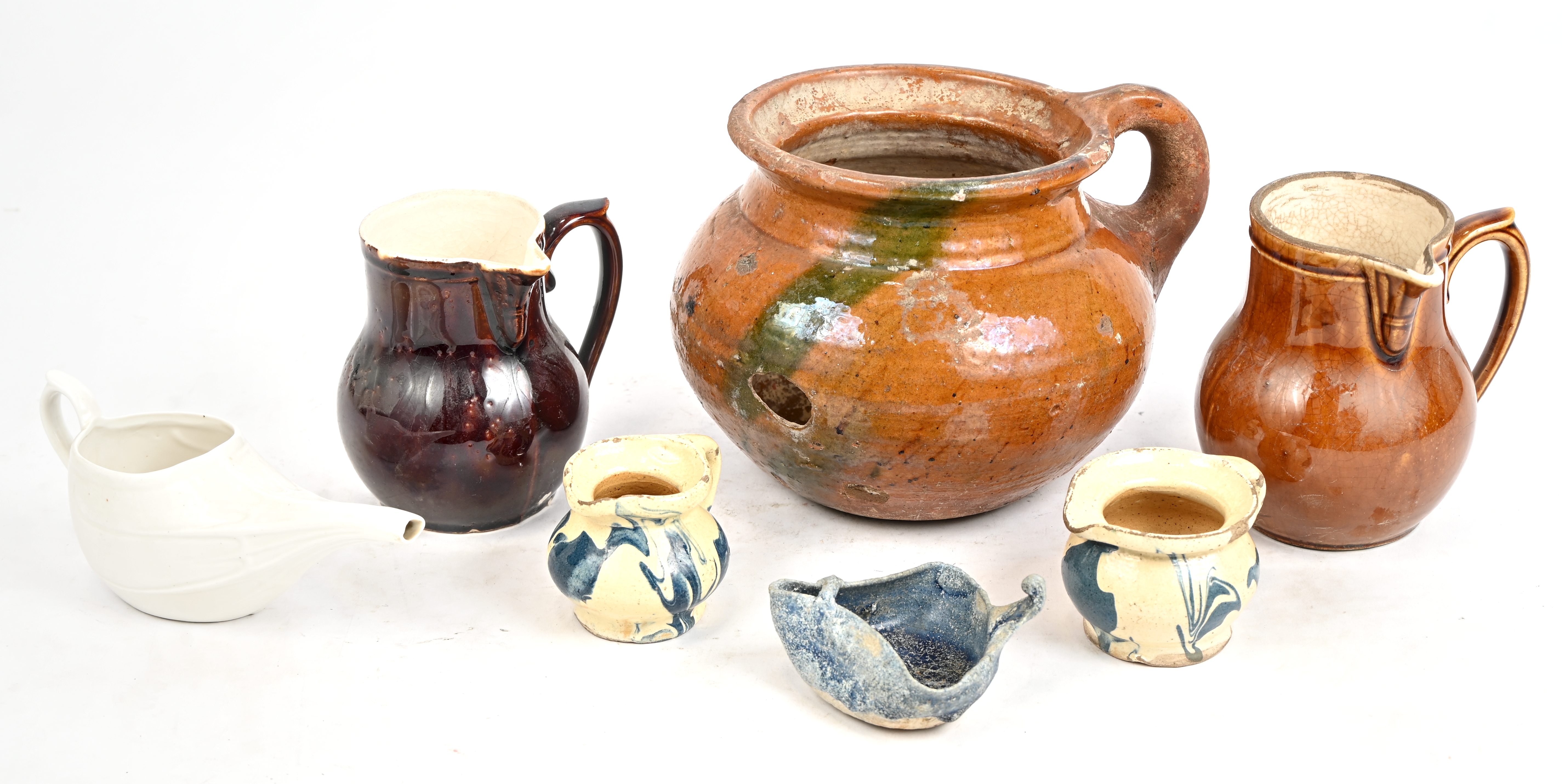 Een lot oude keramische en porseleinen voorwerpen bestaande uit schenkkannetjes. Toegevoegd een oude pot met schade Een lot oude keramische en porseleinen voorwerpen bestaande uit schenkkannetjes. Toegevoegd een oude pot met schade.