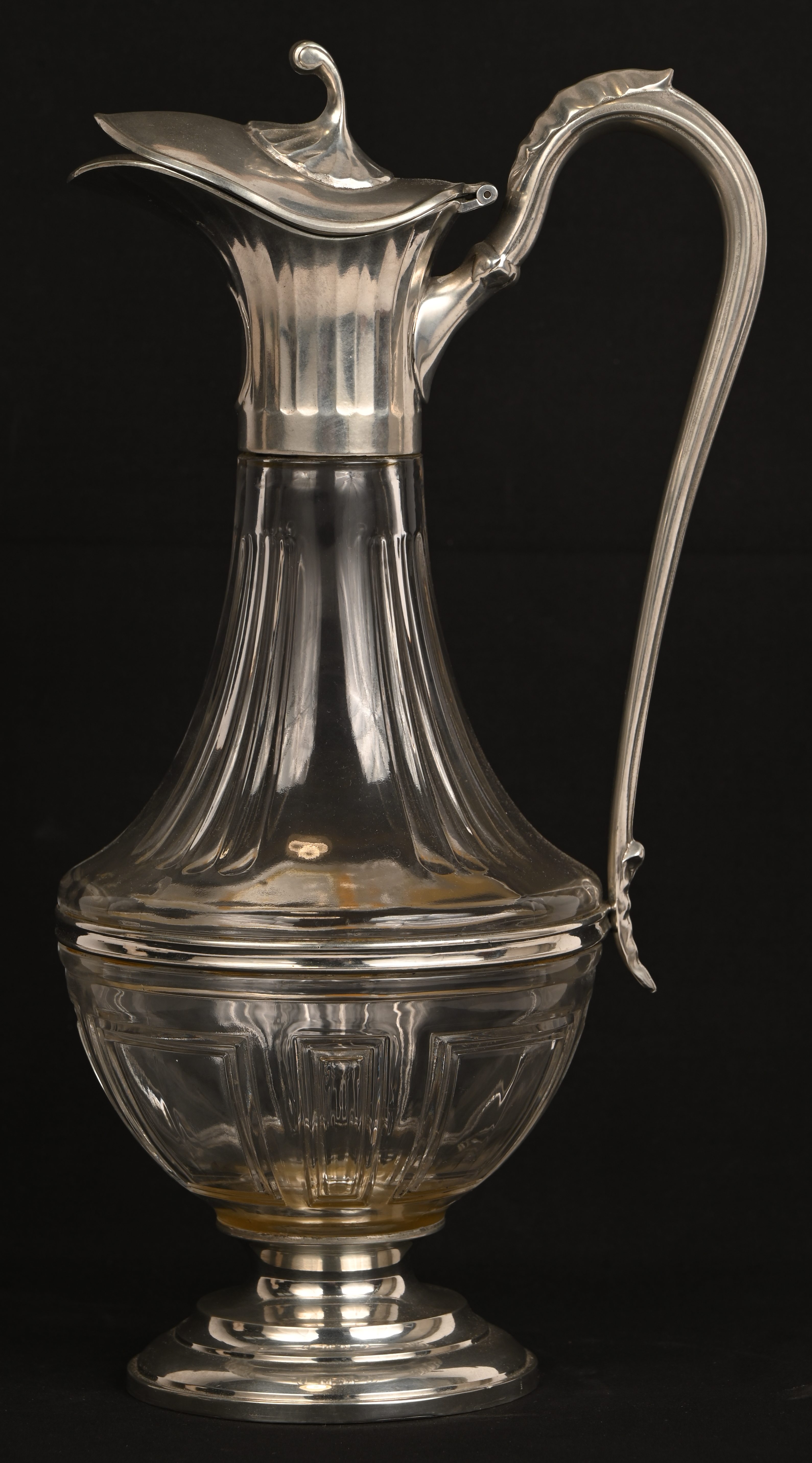 Een glazen decanter met tinnen voet, schenkdeel en handvat Een glazen decanter met tinnen voet, schenkdeel en handvat.