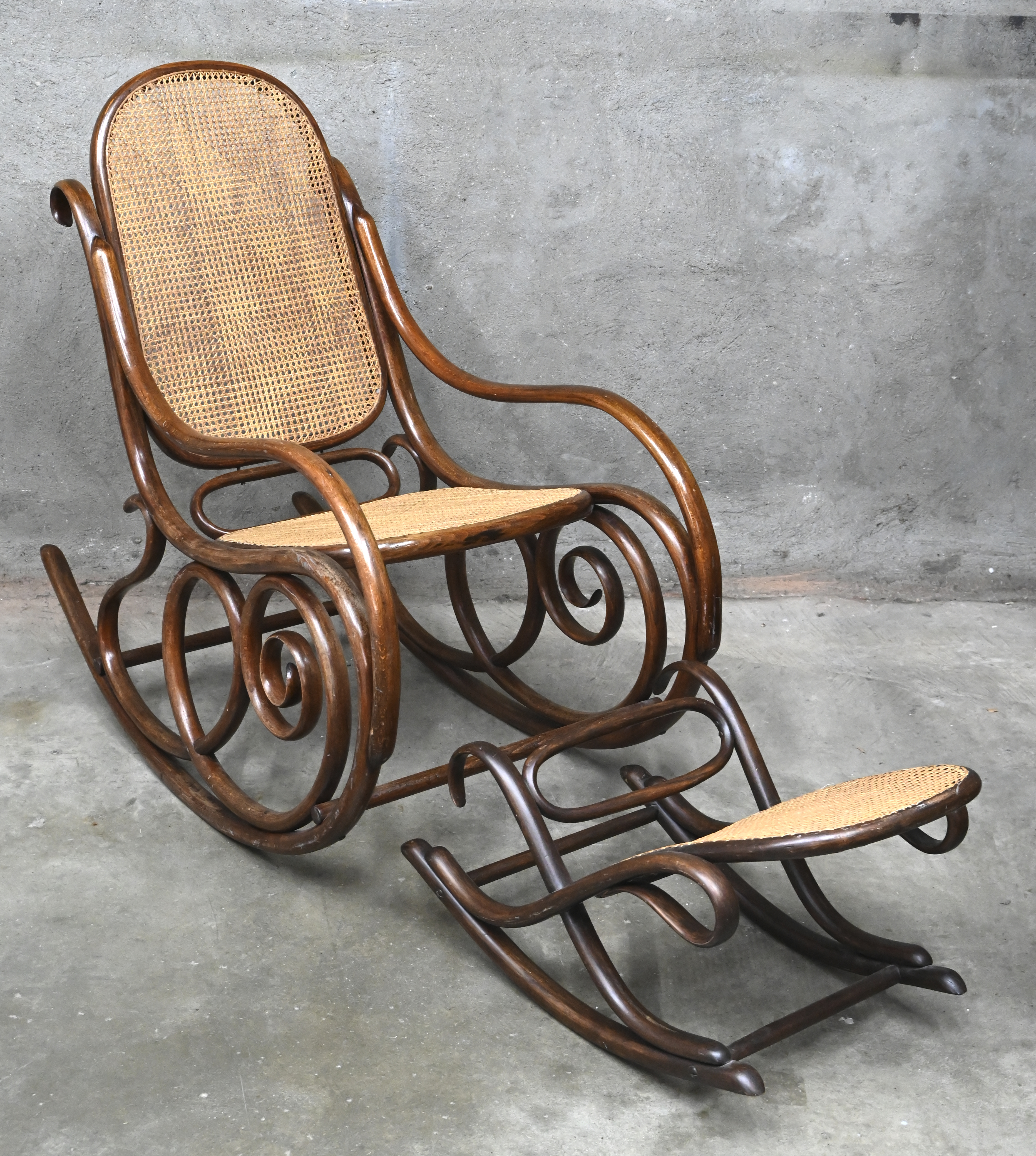 Een ‘bentwood’ schommelstoel in Thonet stijl, toegevoegd een voetbankje met gebarsten deel Een ‘bentwood’ schommelstoel in Thonet stijl, toegevoegd een voetbankje met gebarsten deel.