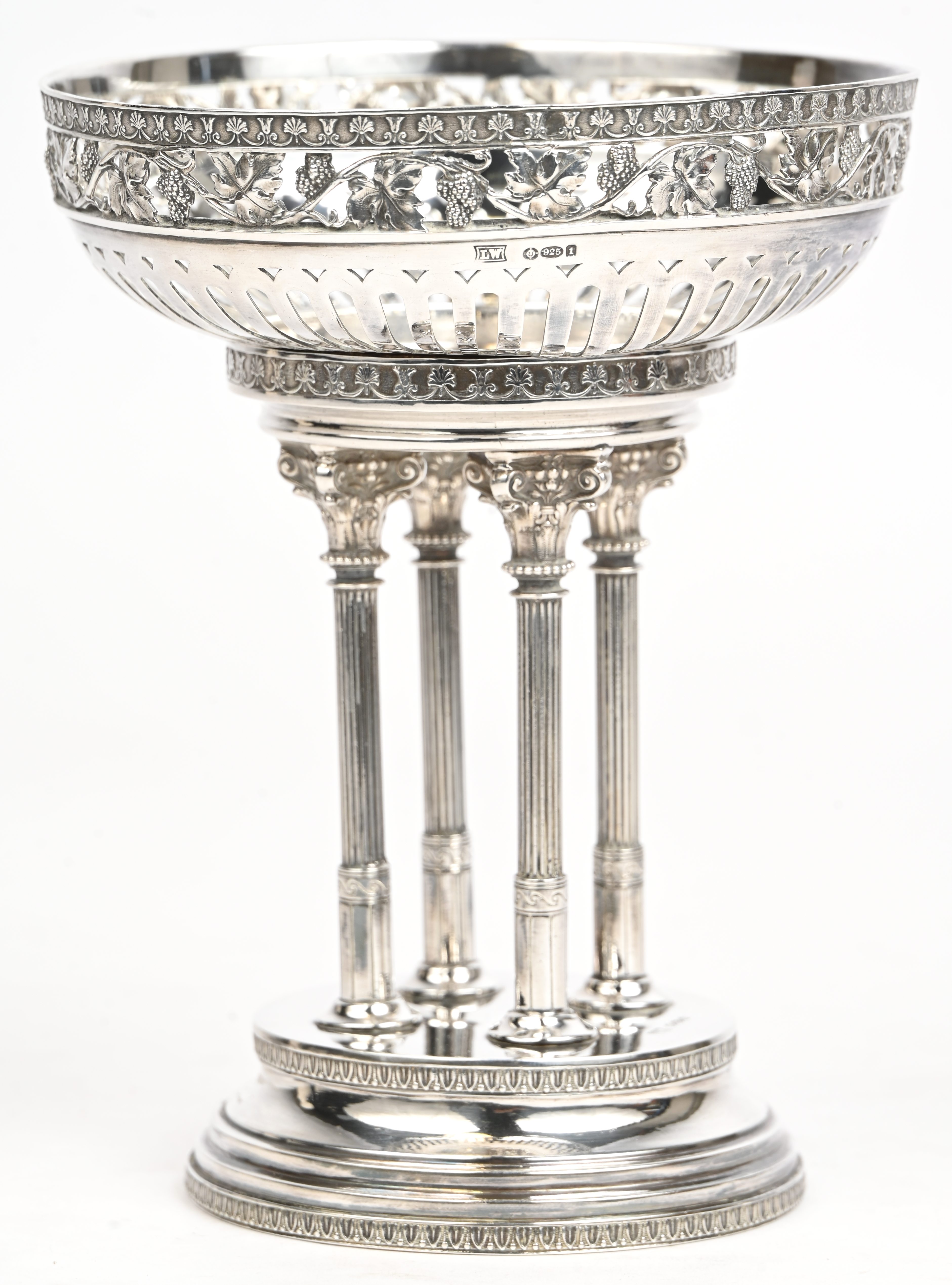 Een zilveren druivenschaal op losse voet, coupe met opengewerkt decor van druivenranken, voet in de vorm van een tempeltje met vier zuiltjes. Londens importmerk, 1906. Gemerkt 925. 505 gram Een zilveren druivenschaal op losse voet, coupe met opengewerkt decor van druivenranken, voet in de vorm van een tempeltje met vier zuiltjes. Londens importmerk, 1906. Gemerkt 925. 505 gram.