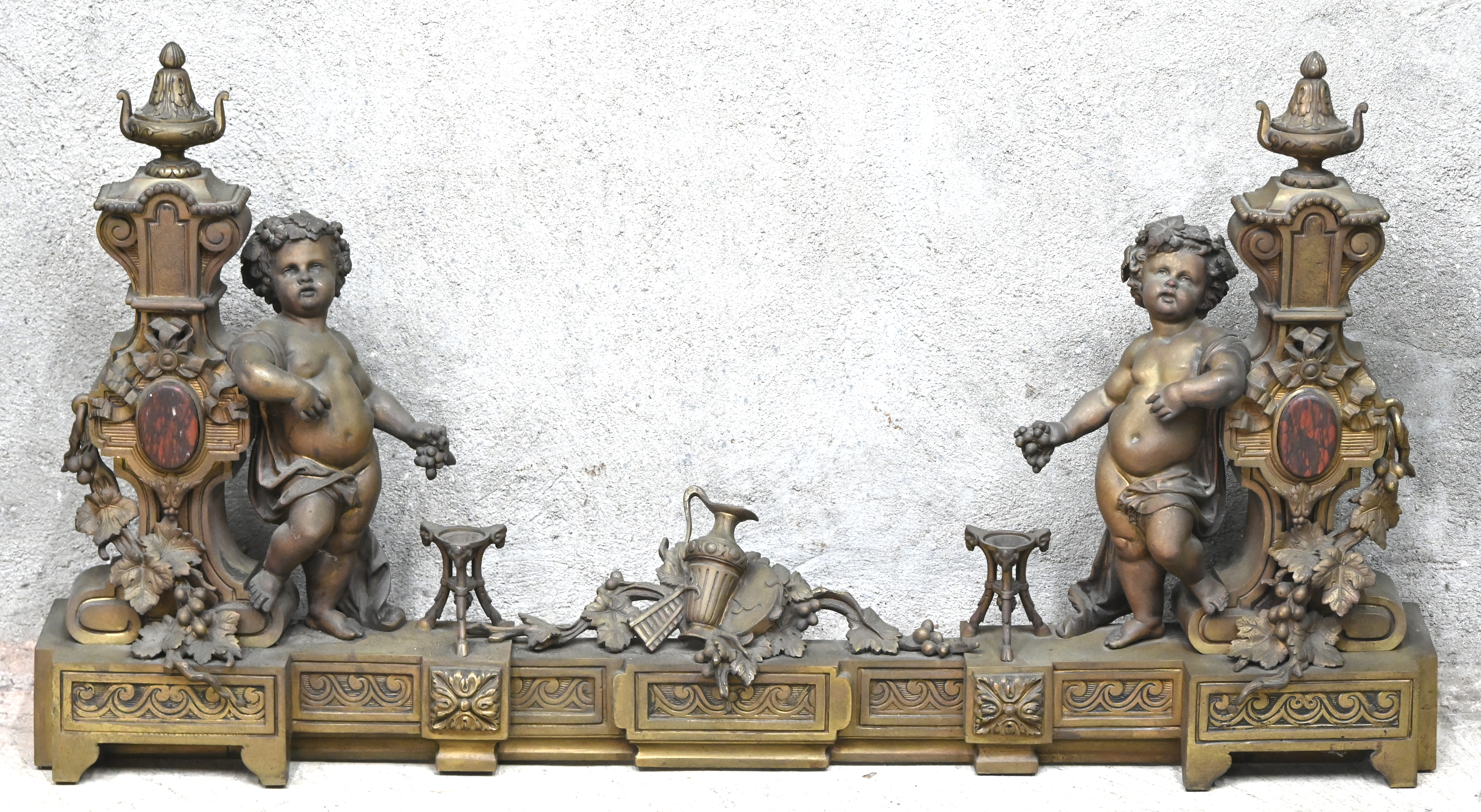 Een bronzen voorzetstuk voor de haard gedecoreerd met putti in neorenaissance-stijl Een bronzen voorzetstuk voor de haard gedecoreerd met putti in neorenaissance-stijl.