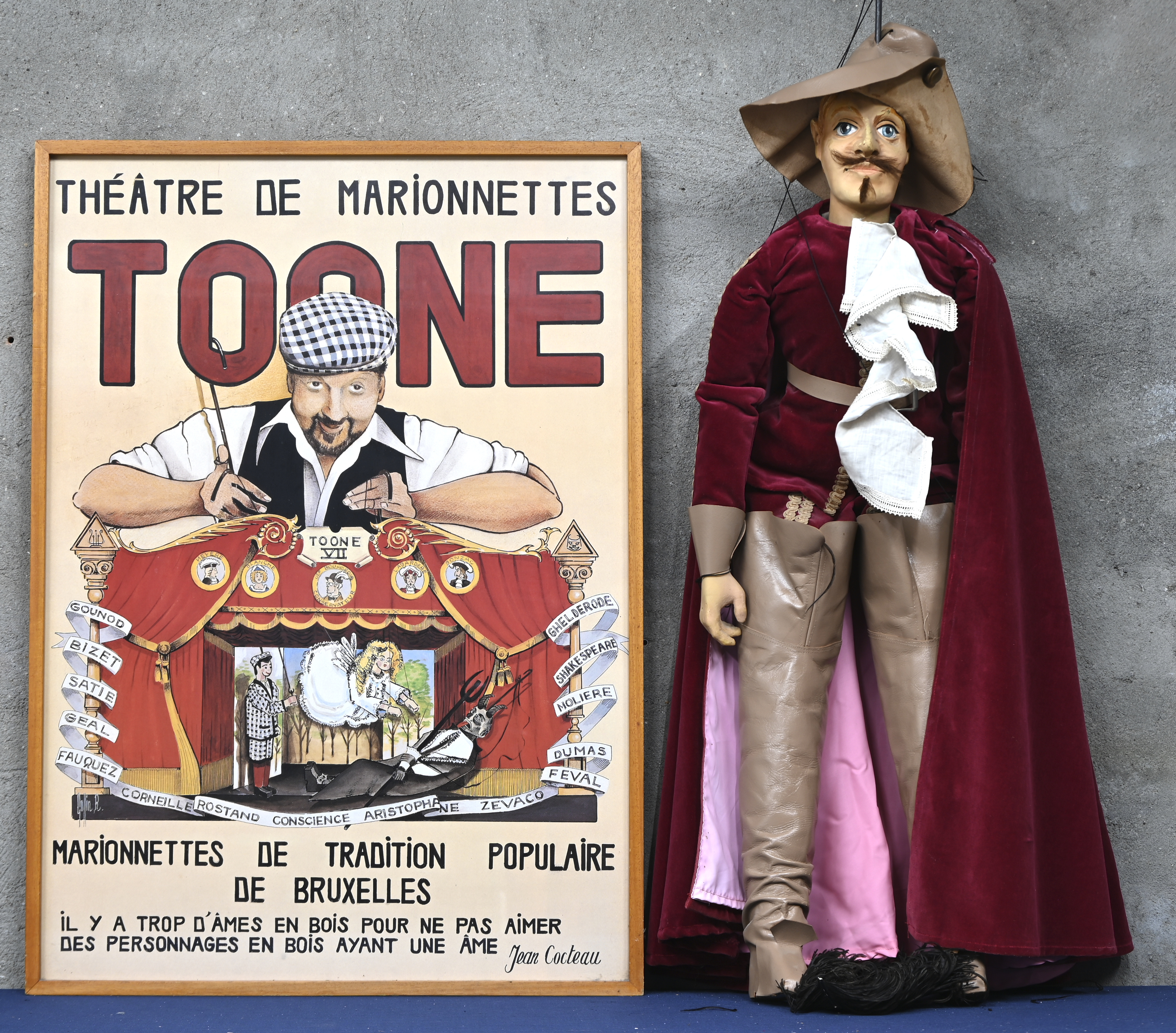 Een grote marionet van een musketier en een ingekaderde affiche van poppentheater Toone Een grote marionet van een musketier en een ingekaderde affiche van poppentheater Toone.