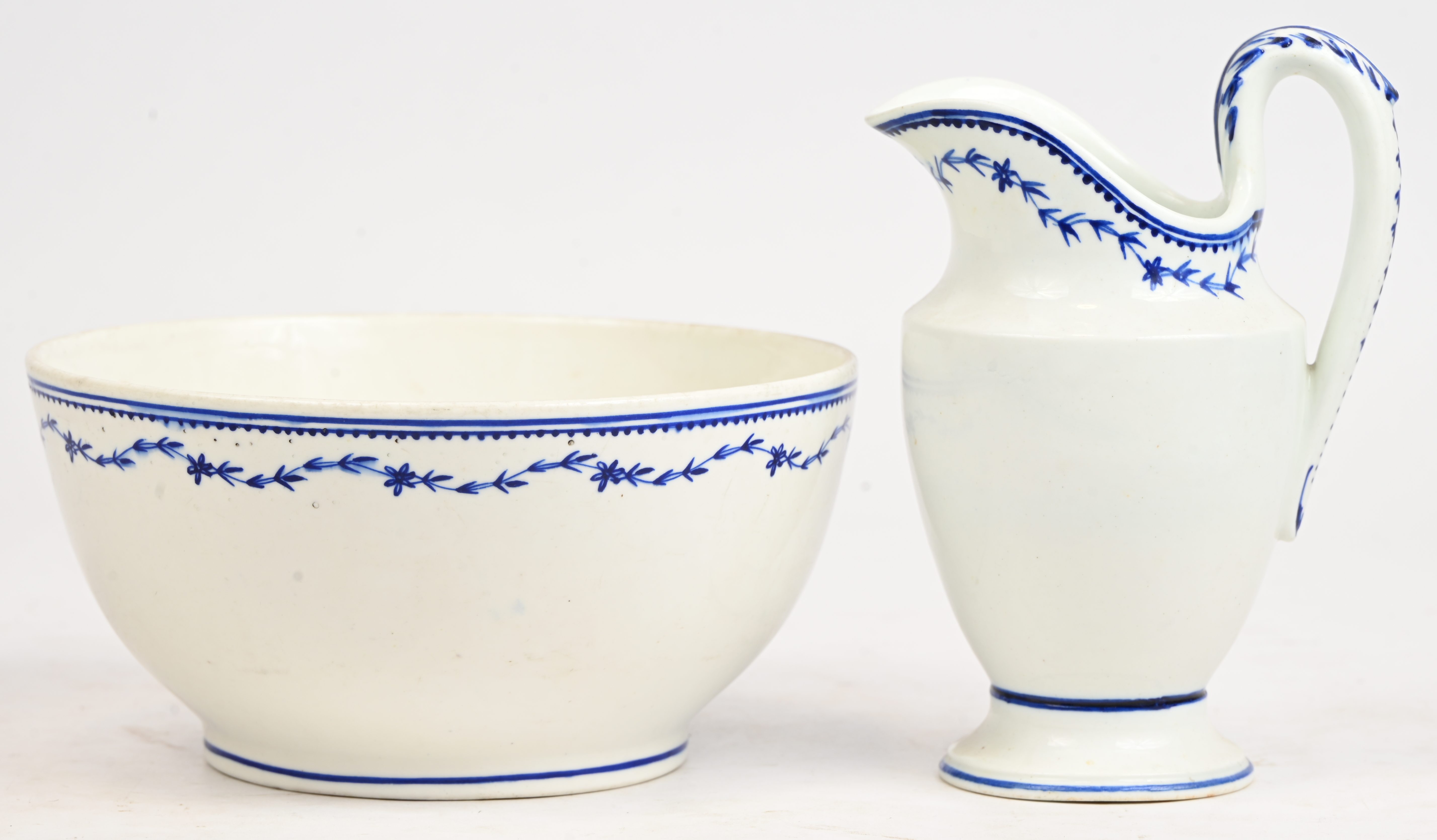 Een melkkannetje met oor en een effen bowl met blauw decor “au laurier fleuri”. Oor van het kannetje versierd met een acanthusblad in reliëf. Bowl gemerkt met een W. en een bijl (?). Doornik, XIXde eeuw Een melkkannetje met oor en een effen bowl met blauw decor “au laurier fleuri”. Oor van het kannetje versierd met een acanthusblad in reliëf. Bowl gemerkt met een W. en een bijl (?). Doornik, XIXde eeuw.