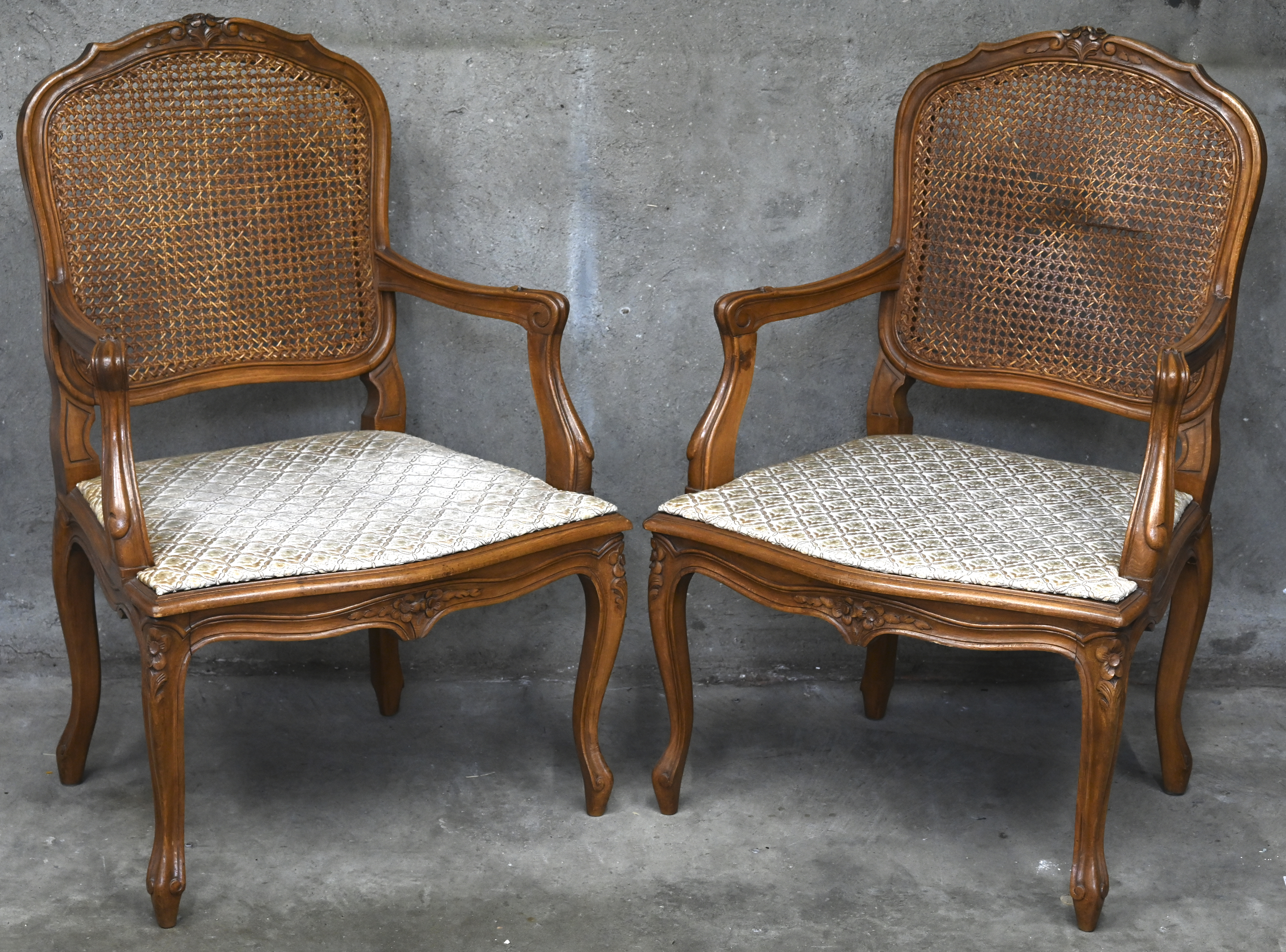 Een paar gesculpteerde houten armstoelen met gestoffeerde zitting en rieten rugleuning Een paar gesculpteerde houten armstoelen met gestoffeerde zitting en rieten rugleuning.