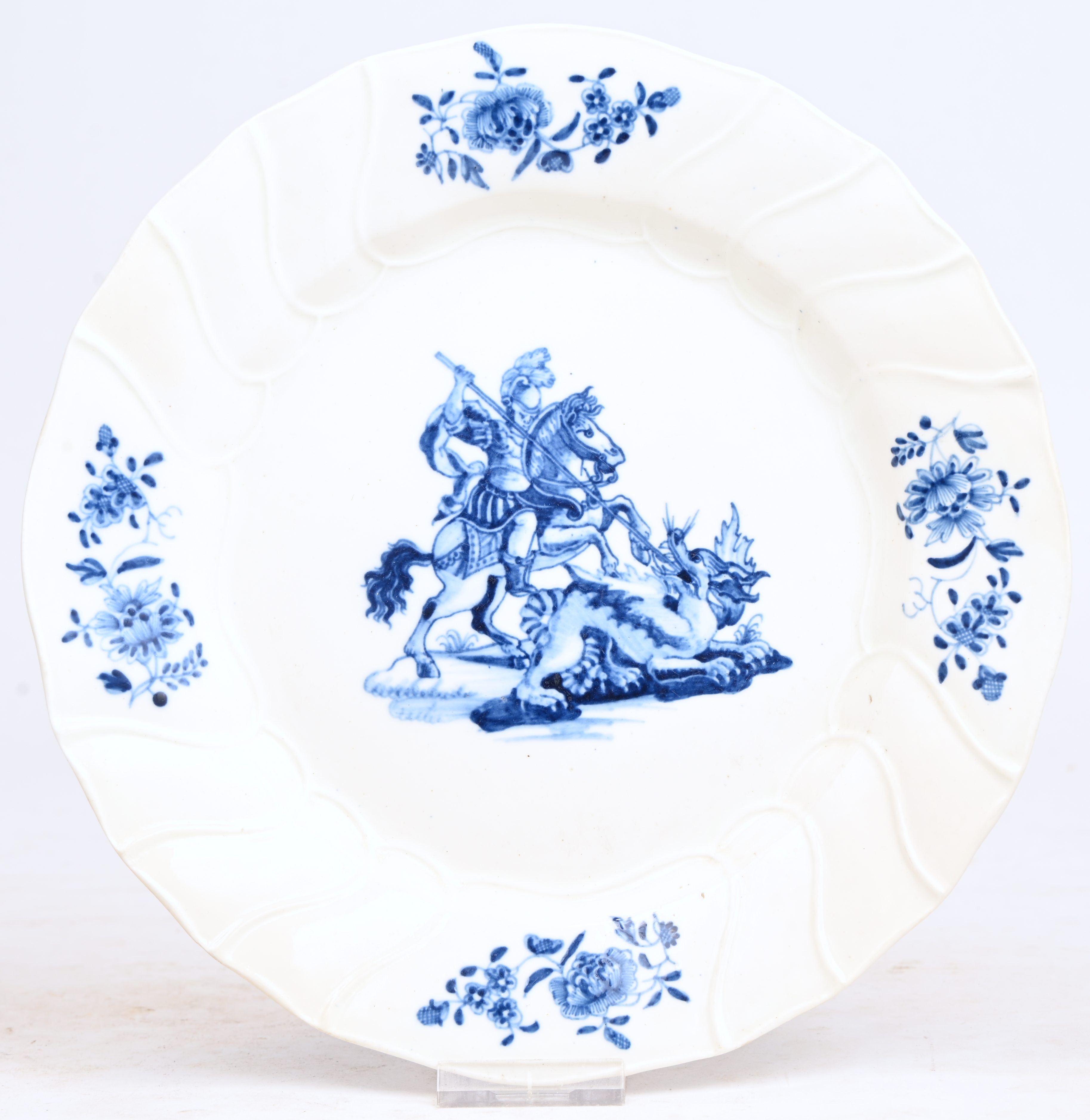 Een bord met blauw decor van een Sint-Joris op het plat en vier bloementuilen op de vleugel. Getorste ribben, licht gechantourneerde rand. Onderaan gemerkt L.B. in blauw onder glazuur. Doornik, XVIIIde eeuw Een bord met blauw decor van een Sint-Joris op het plat en vier bloementuilen op de vleugel. Getorste ribben, licht gechantourneerde rand. Onderaan gemerkt L.B. in blauw onder glazuur. Doornik, XVIIIde eeuw.