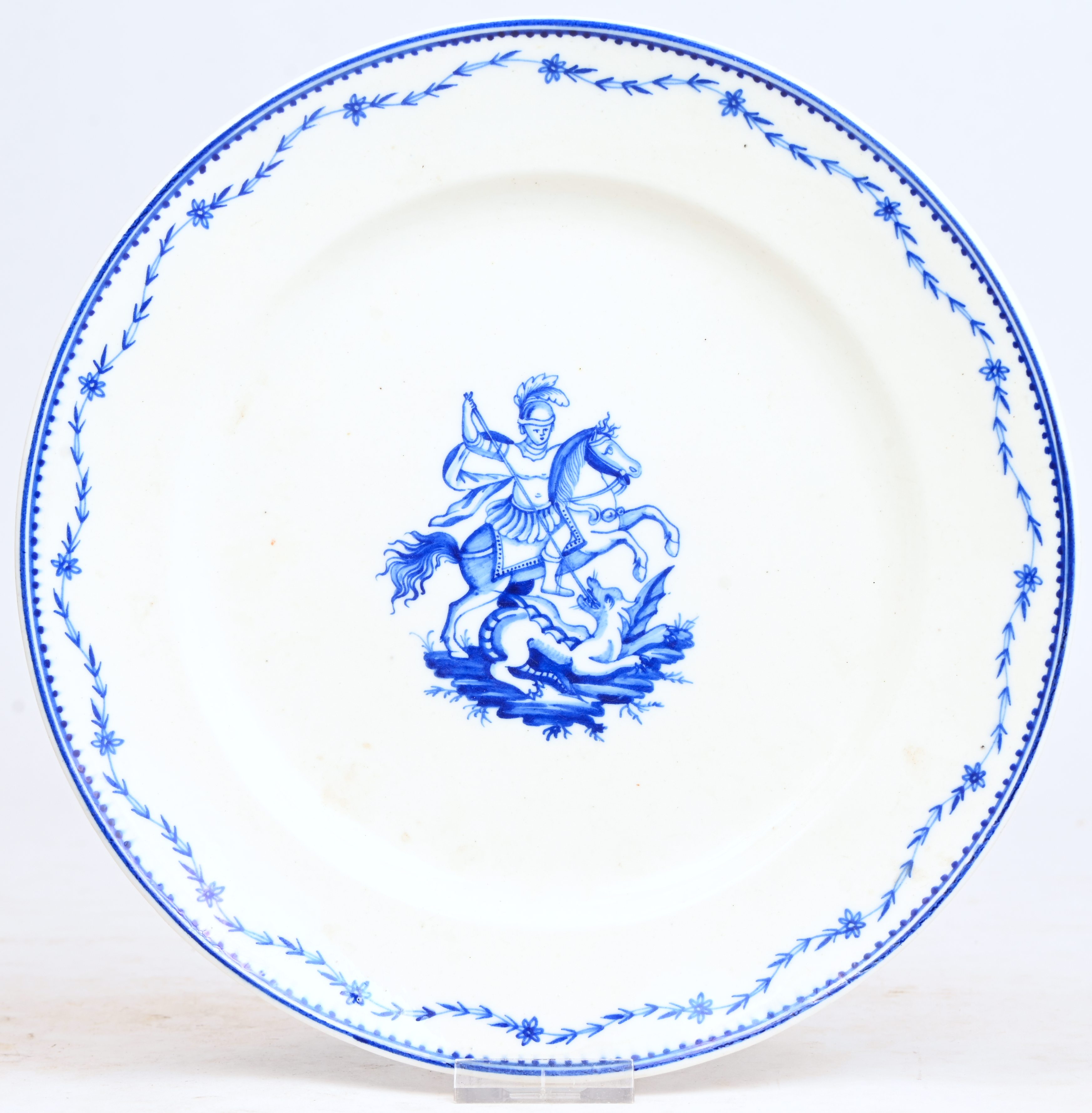 Een bord met blauw decor van een Sint-Joris op het plat. Rand met Laurier Fleuri motief. Onderaan gemerkt A. in blauw onder glazuur. Doornik, XIXde eeuw Een bord met blauw decor van een Sint-Joris op het plat. Rand met Laurier Fleuri motief. Onderaan gemerkt A. in blauw onder glazuur. Doornik, XIXde eeuw.