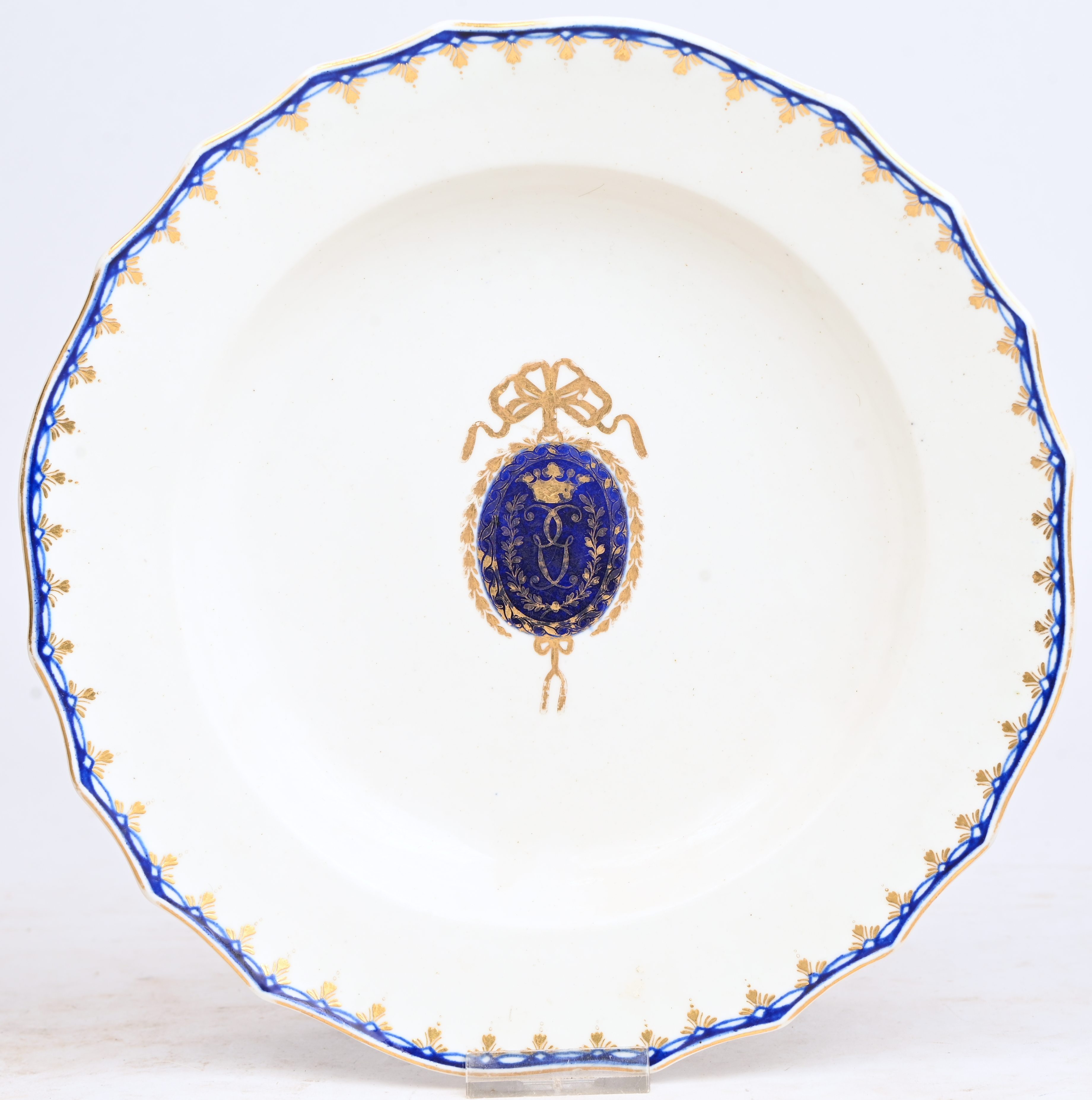 Bord met een blauw Lodewijk XVI medaillondecor met wapen van familie Gouthals, gehoogd met goud. Rand versierd in blauw en met vergulde bloemenguirlande, gechantourneerde rand. Doornik, XVIIIde eeuw Bord met een blauw Lodewijk XVI medaillondecor met wapen van familie Gouthals, gehoogd met goud. Rand versierd in blauw en met vergulde bloemenguirlande, gechantourneerde rand. Doornik, XVIIIde eeuw.