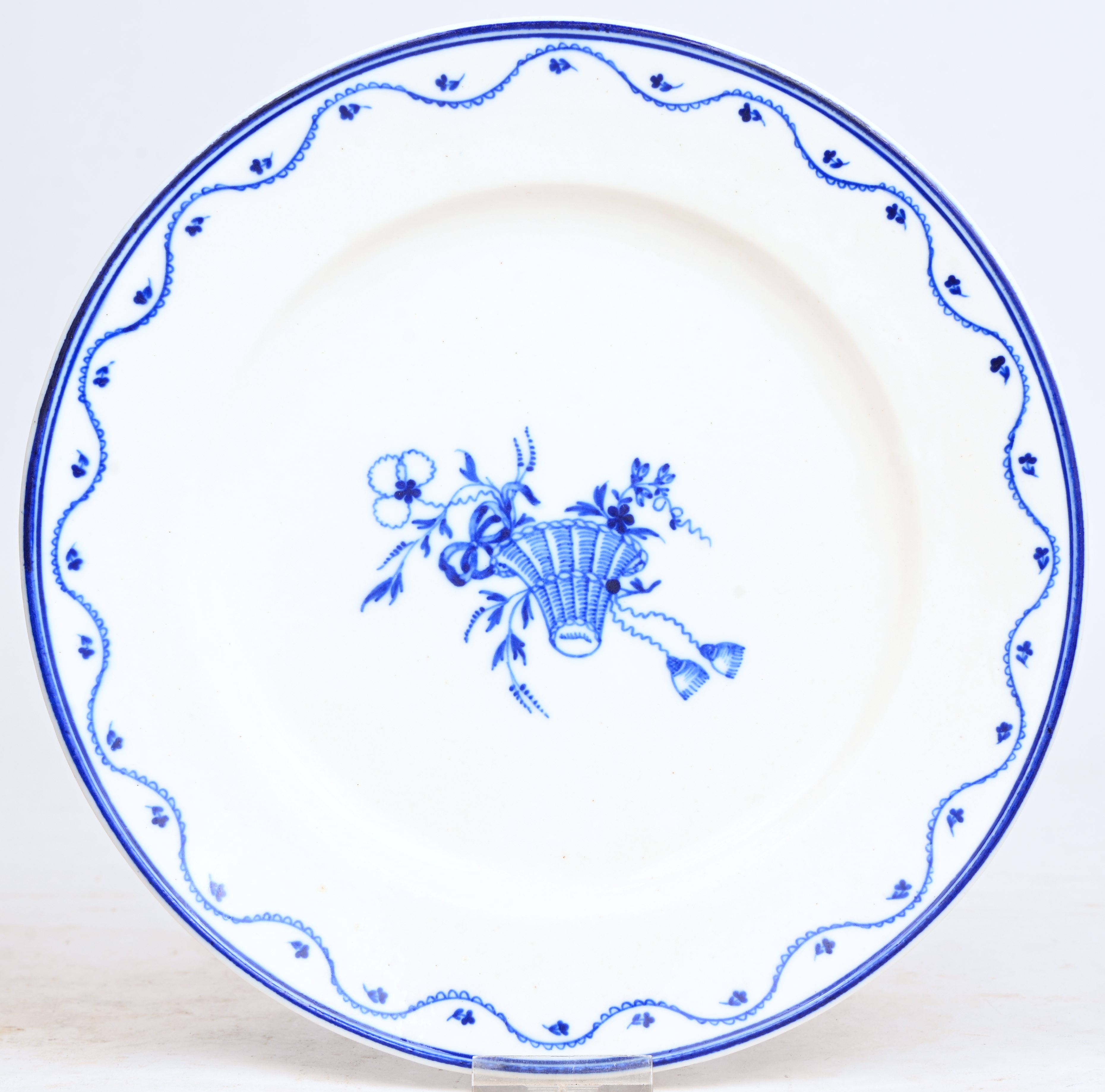 Bord met een blauw decor met bloemenkorf op het plat. Op de rand gegolfde lijn met kleine bloemen. Onderaan gemerkt K in blauw onder glazuur. Doornik, omstreeks 1800 Bord met een blauw decor met bloemenkorf op het plat. Op de rand gegolfde lijn met kleine bloemen. Onderaan gemerkt K in blauw onder glazuur. Doornik, omstreeks 1800.