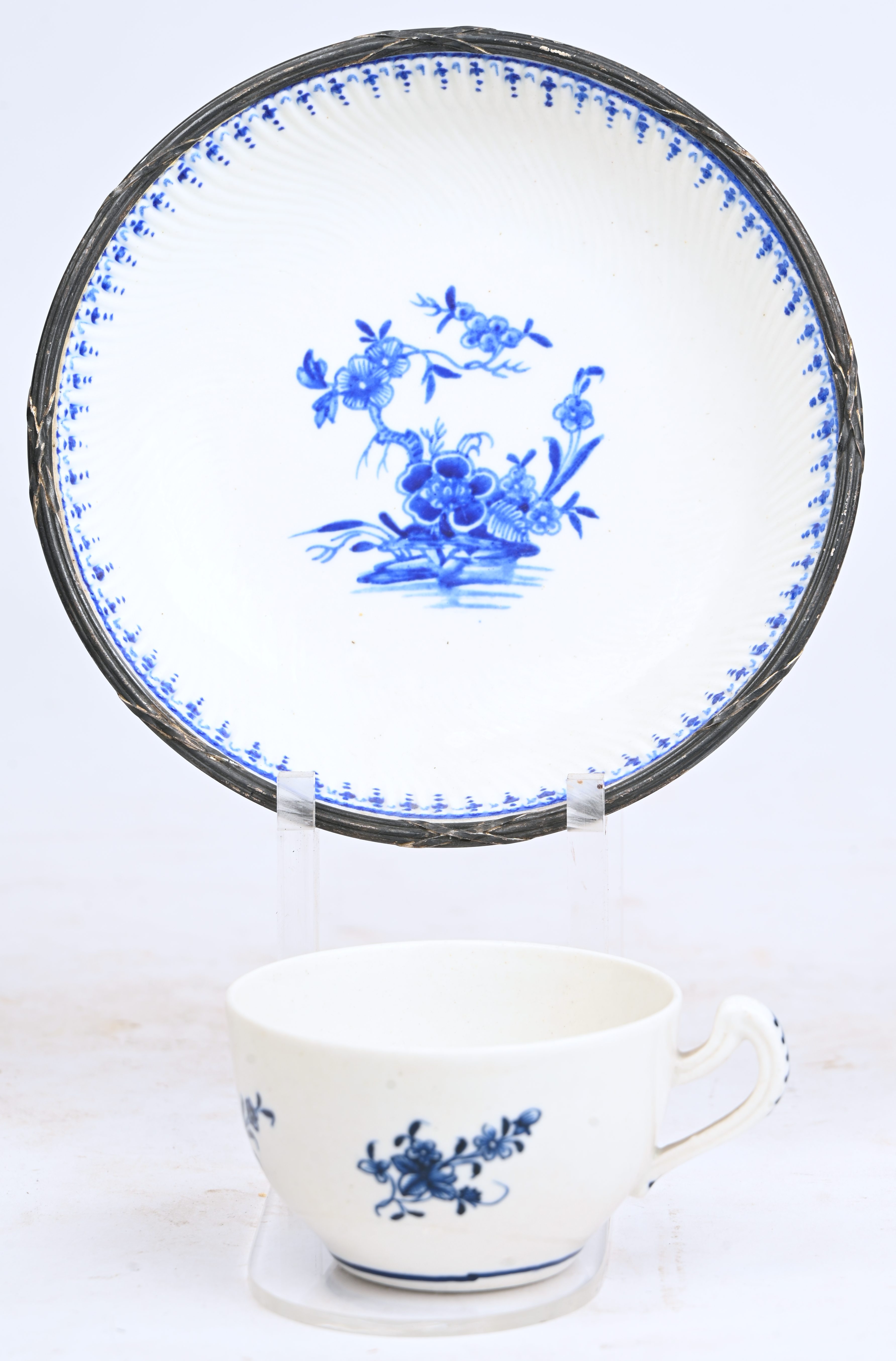 Een mokkakopje met decor “Ronda” op het plat en en schoteltje met 1000 ribben-motief, eveneens met “Ronda”-decor en met een bloemenguirlande. Met een gedreven zilveren randje. Doornik, einde XVIIIde eeuw Een mokkakopje met decor “Ronda” op het plat en en schoteltje met 1000 ribben-motief, eveneens met “Ronda”-decor en met een bloemenguirlande. Met een gedreven zilveren randje. Doornik, einde XVIIIde eeuw.