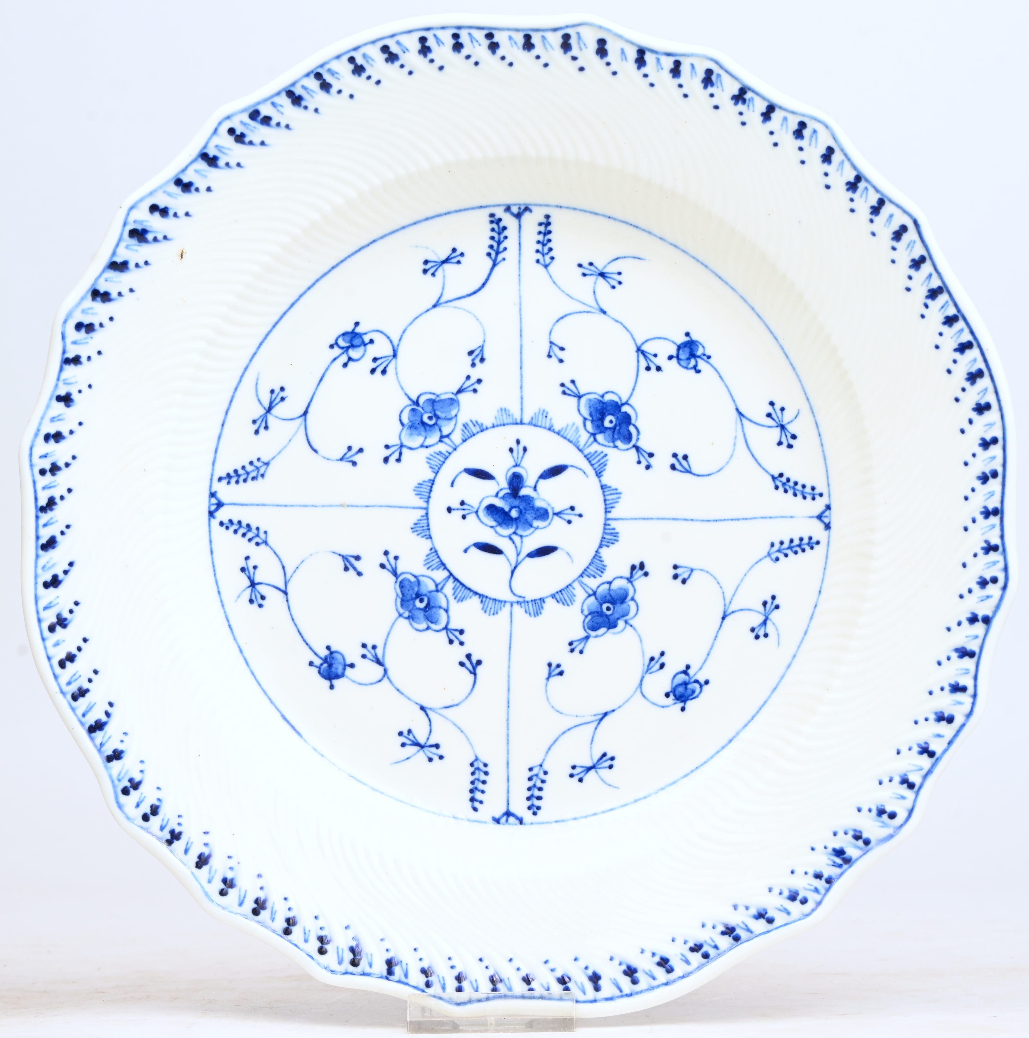 Kaasbord van zachte pasta met een “immortelle de Saxe”-décor en een randversiering “à la pensée” en met “1000 getorste ribben” in reliëf. Gechantourneerde rand. Gemerkt met de zwaarden en de kruisjes. Doornik, XIXde eeuw Kaasbord van zachte pasta met een “immortelle de Saxe”-décor en een randversiering “à la pensée” en met “1000 getorste ribben” in reliëf. Gechantourneerde rand. Gemerkt met de zwaarden en de kruisjes. Doornik, XIXde eeuw.