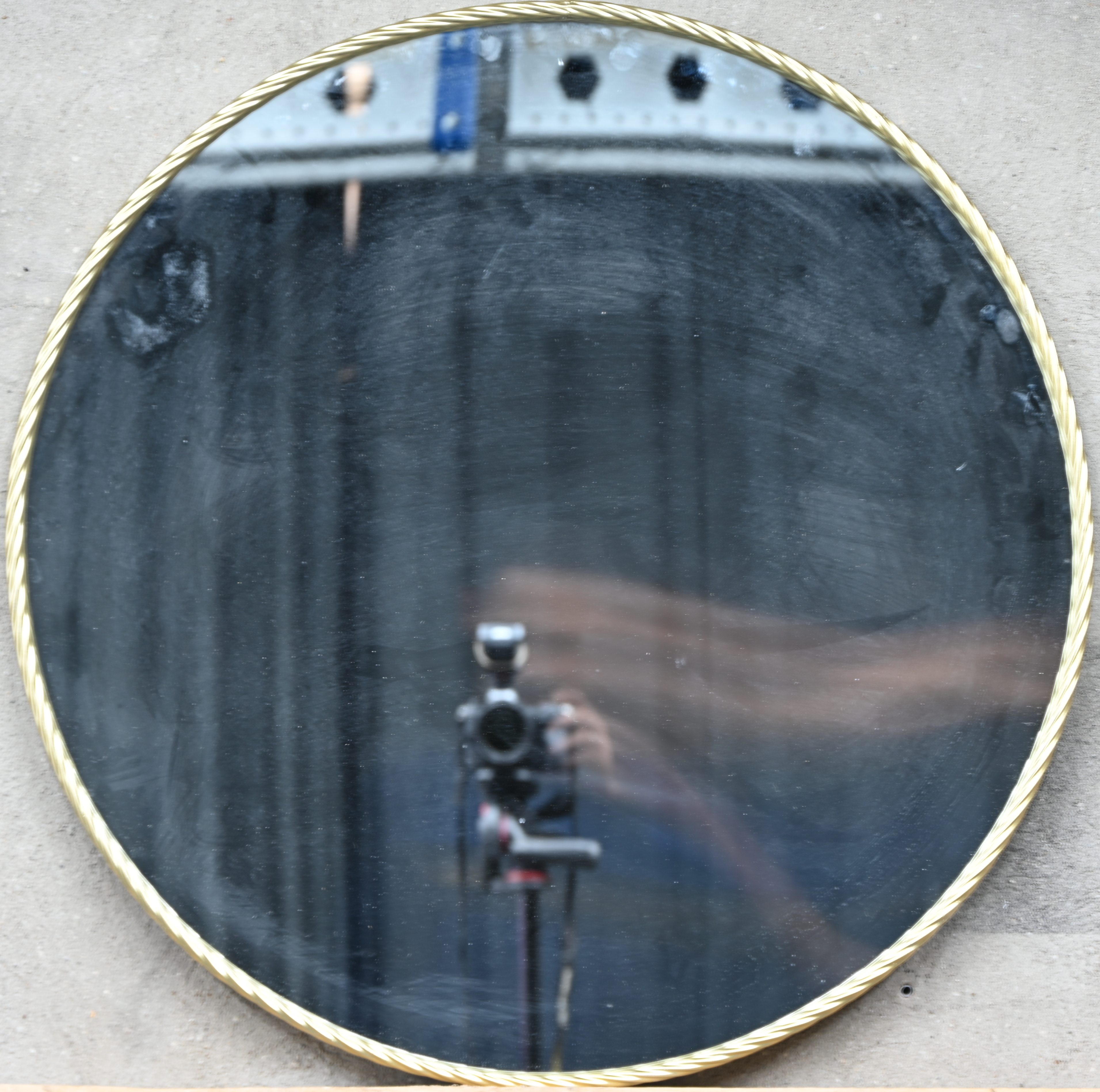 Een grote ronde spiegel met een goudkleurige metalen kader Een grote ronde spiegel met een goudkleurige metalen kader.